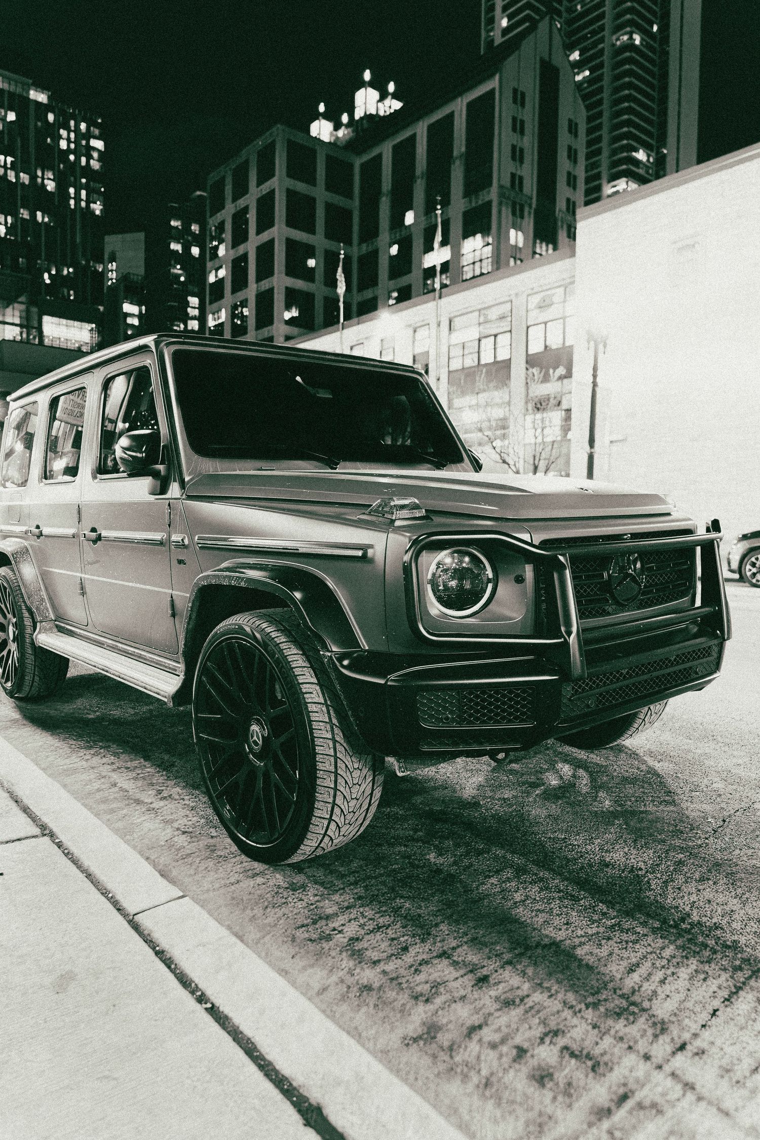 Vintage-style black and white photo of luxury SUVs parked on city street at night.