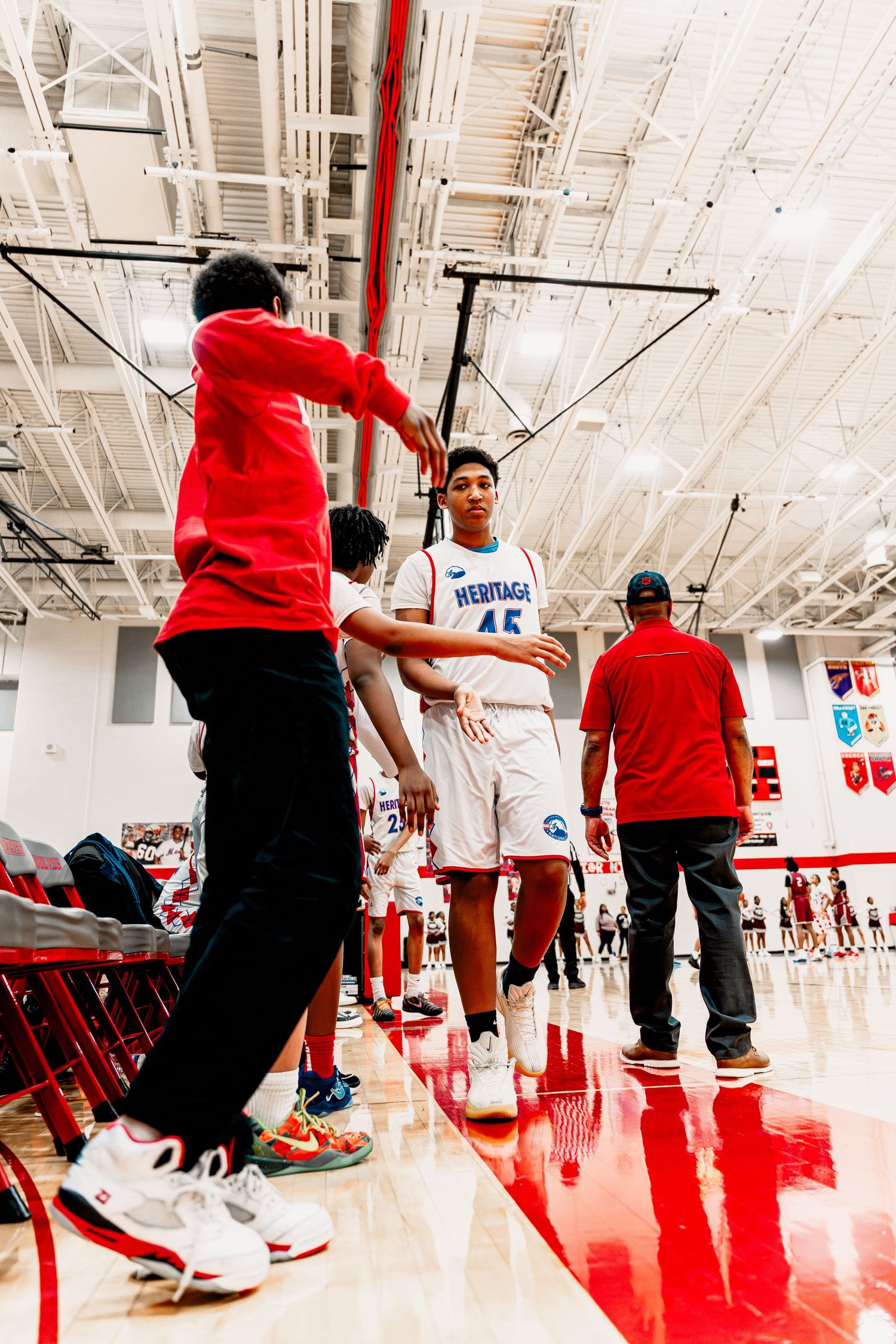 Basketball players practice defensive footwork drills on a shiny red court during training.