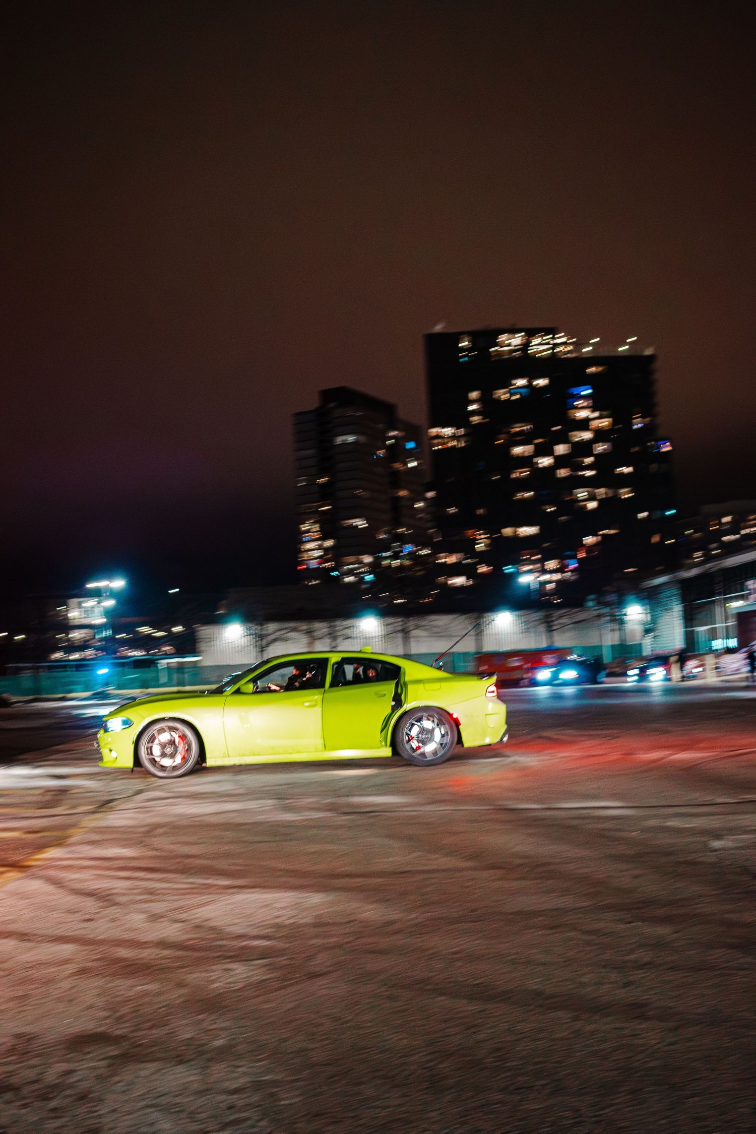 Neon yellow sports car illuminated at night against a dark cityscape with glowing building lights.