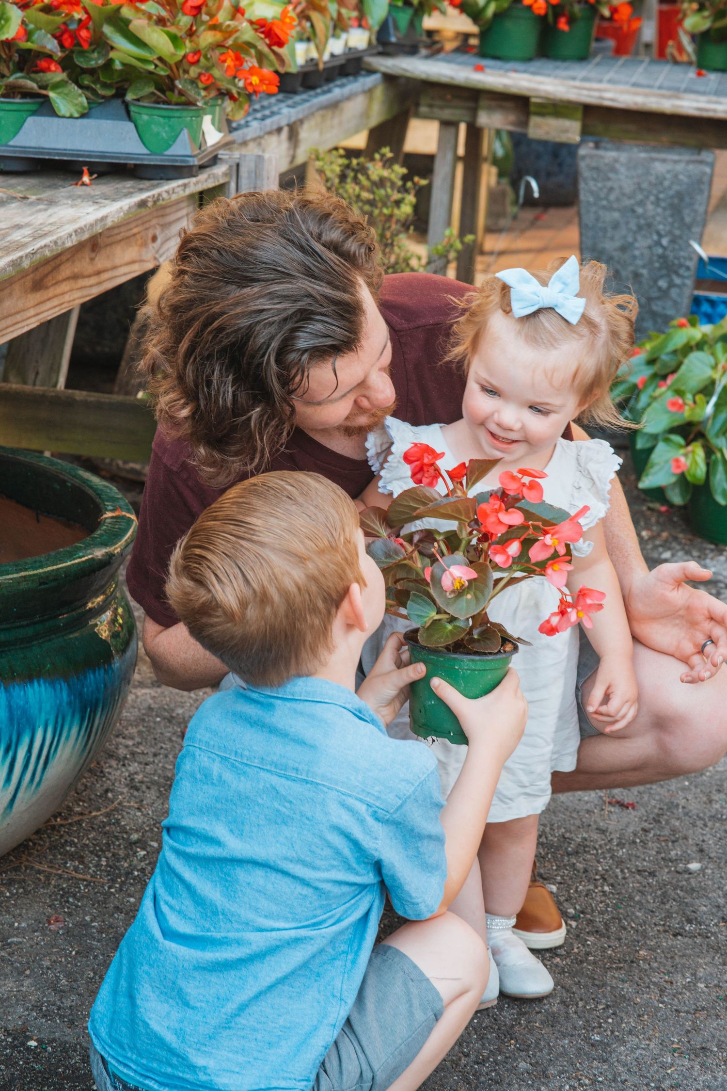 A group examines flowering plants together in a garden greenhouse setting.