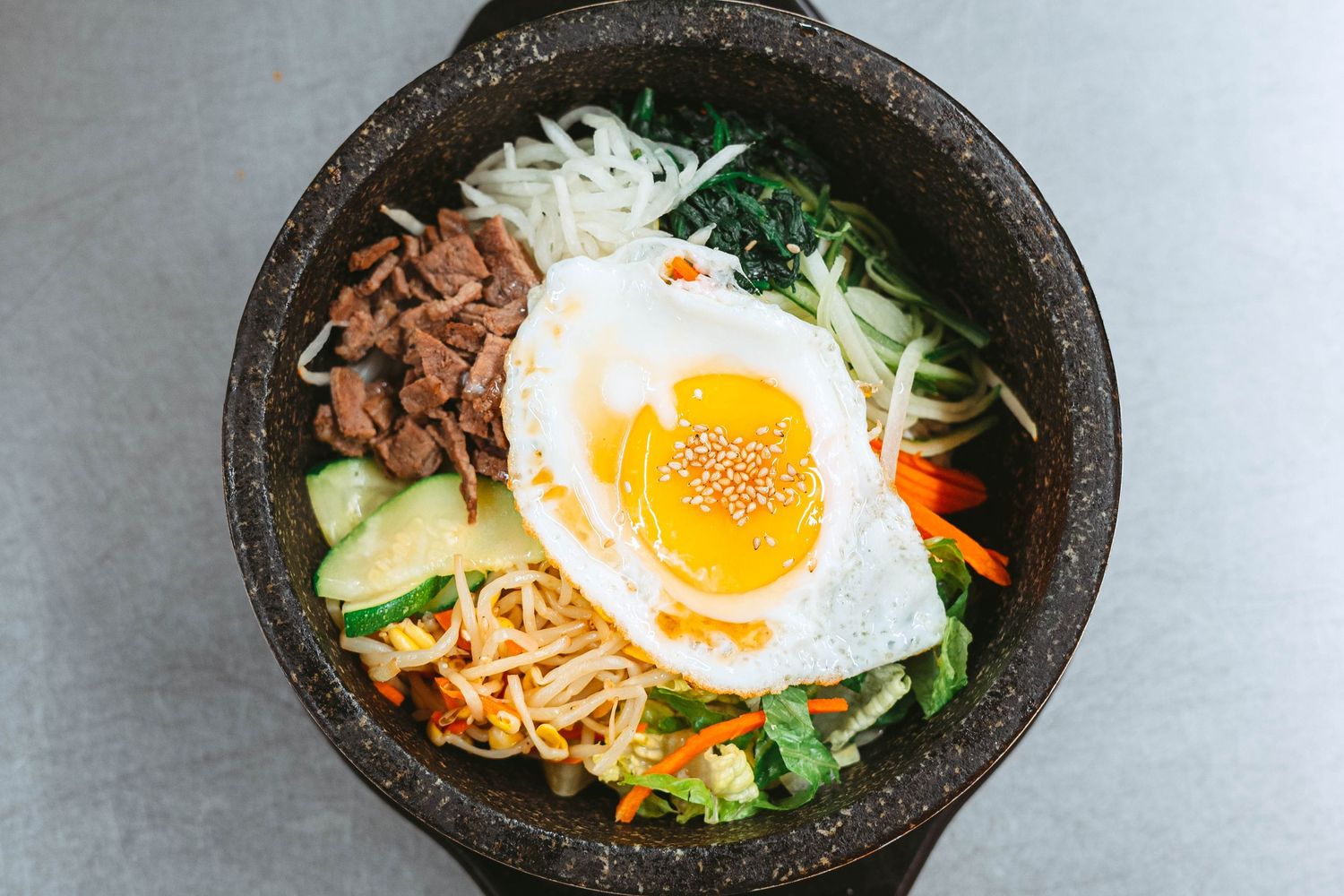 Korean bibimbap bowl with sunny side up egg, vegetables, and meat served in a traditional stone bowl.