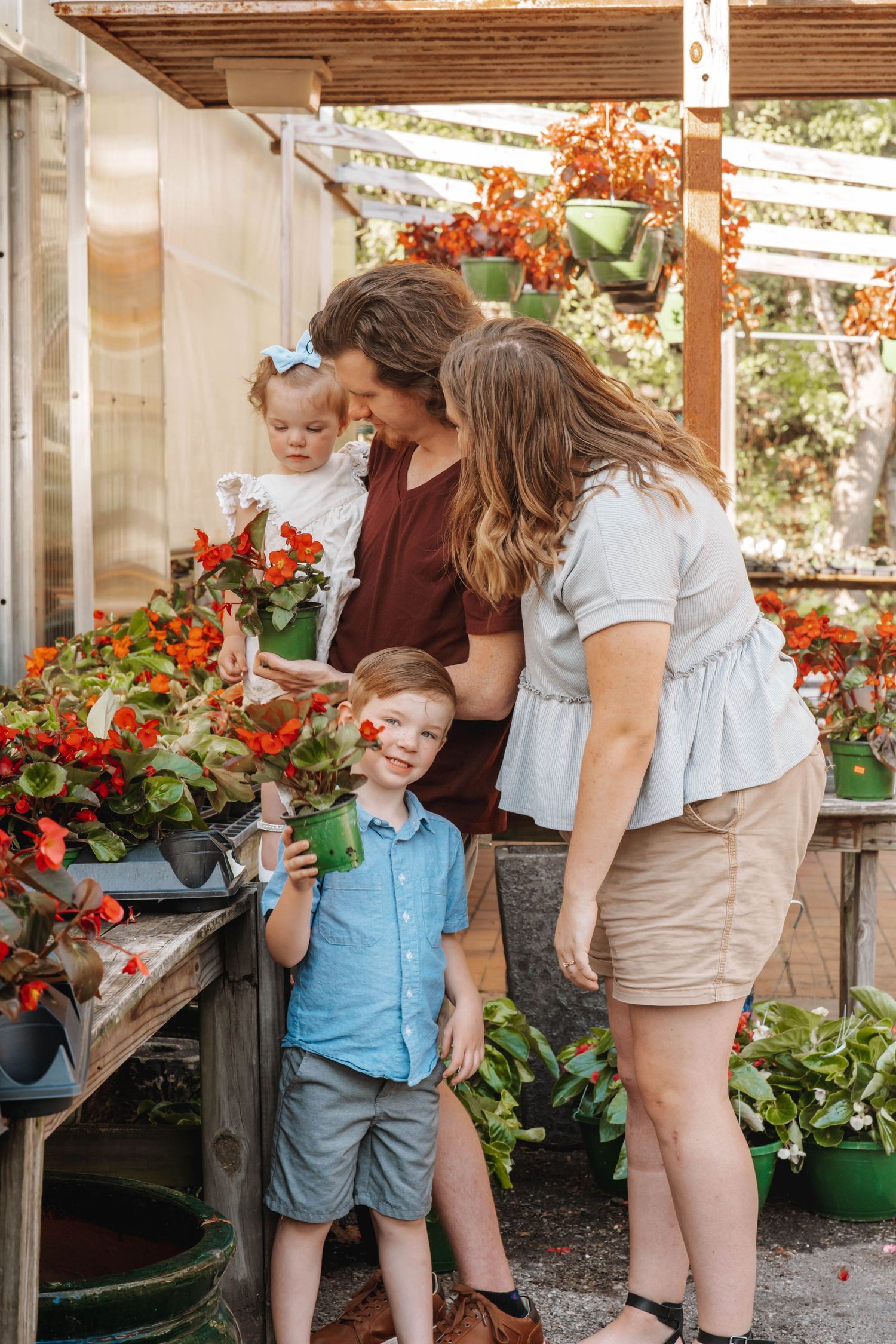 Family enjoying time together in greenhouse surrounded by red flowers.