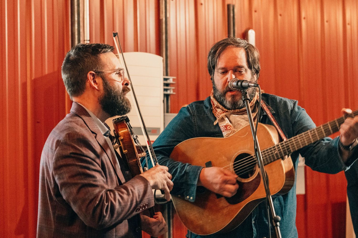 Musicians performing with instruments against vibrant orange background.