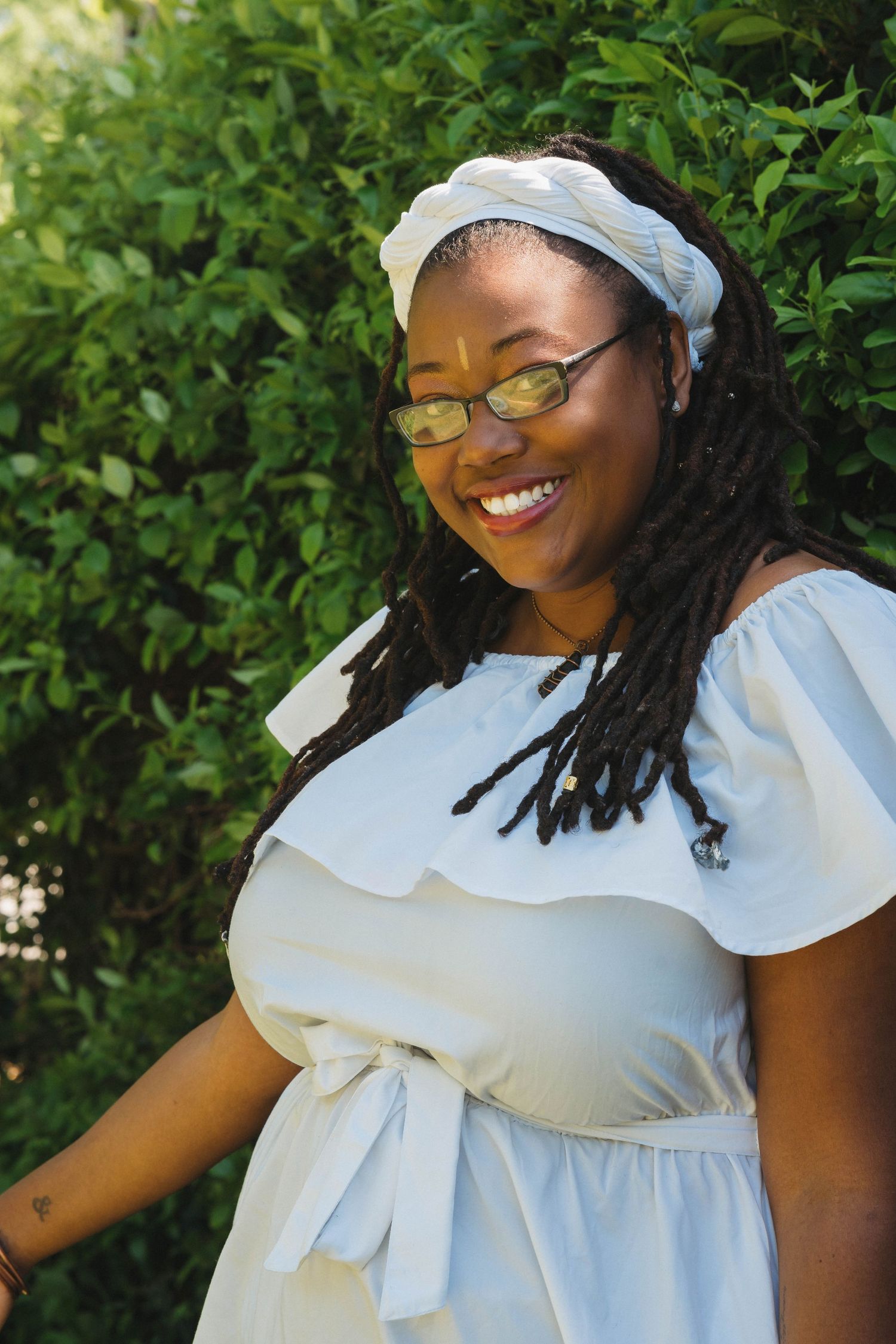 Natural light portraits featuring white ruffle dress and head wrap in garden setting.