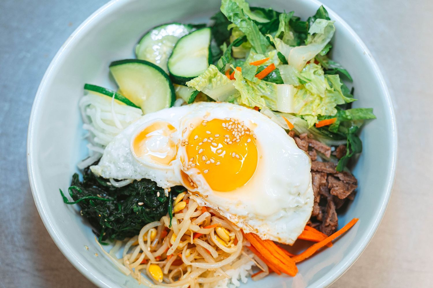 Korean bibimbap bowls with fresh vegetables, sunny side up eggs, rice and colorful toppings arranged in a row.
