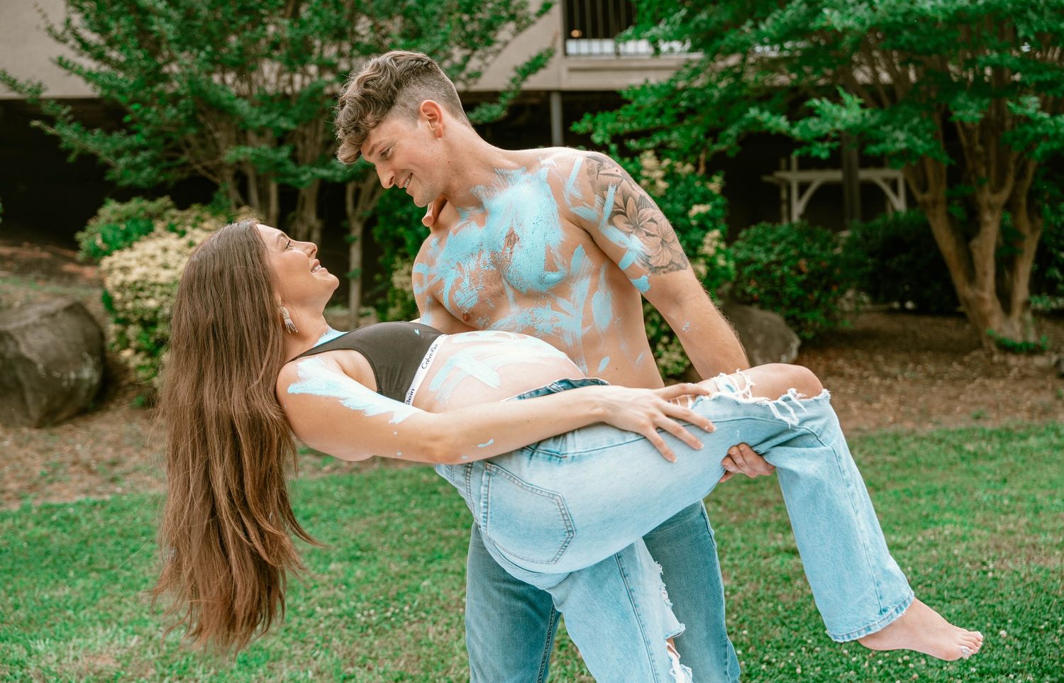A couple shares a romantic moment in a lush green garden setting during a summer photoshoot.