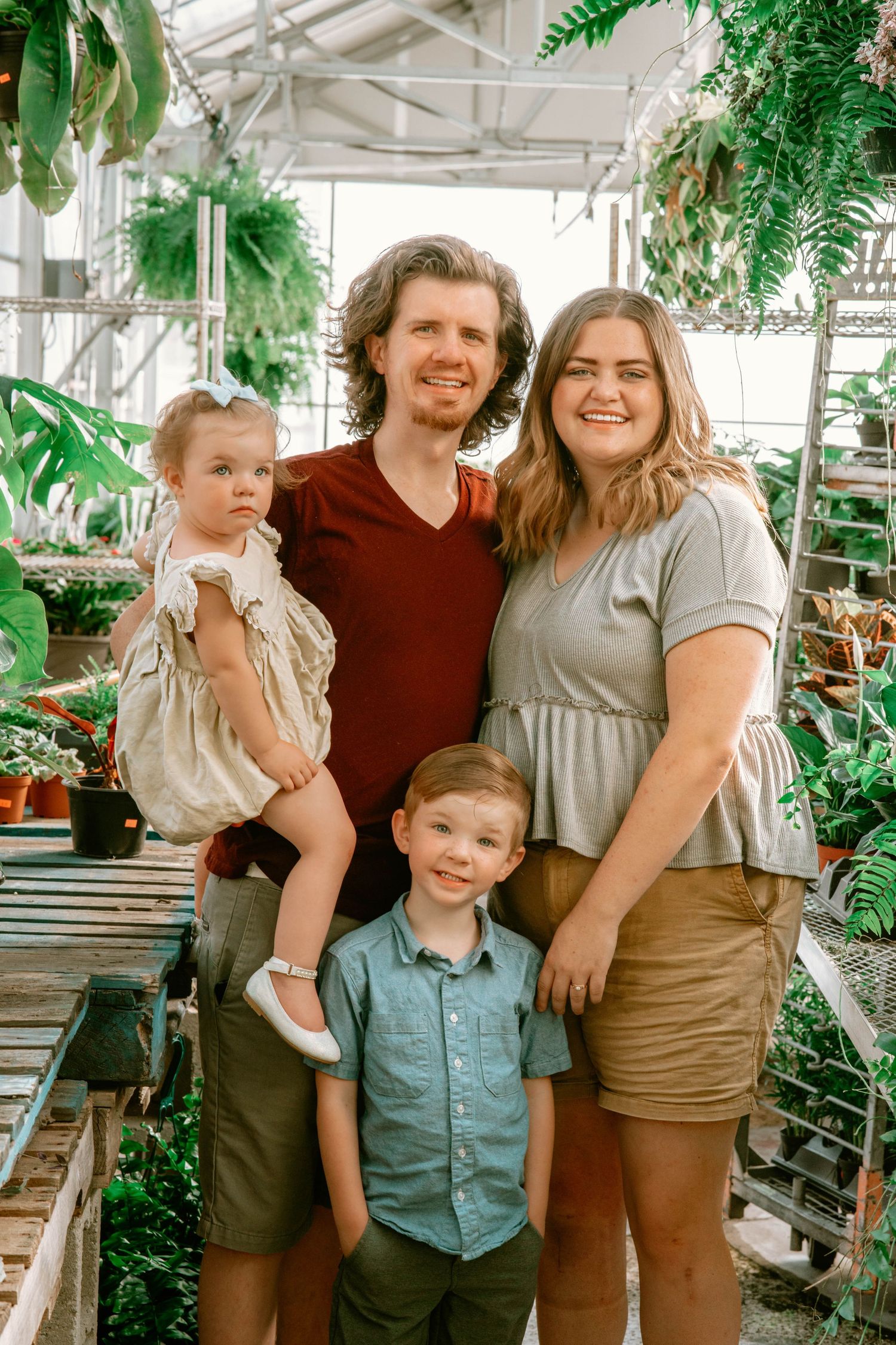 A family poses together in a greenhouse surrounded by lush plants and greenery.