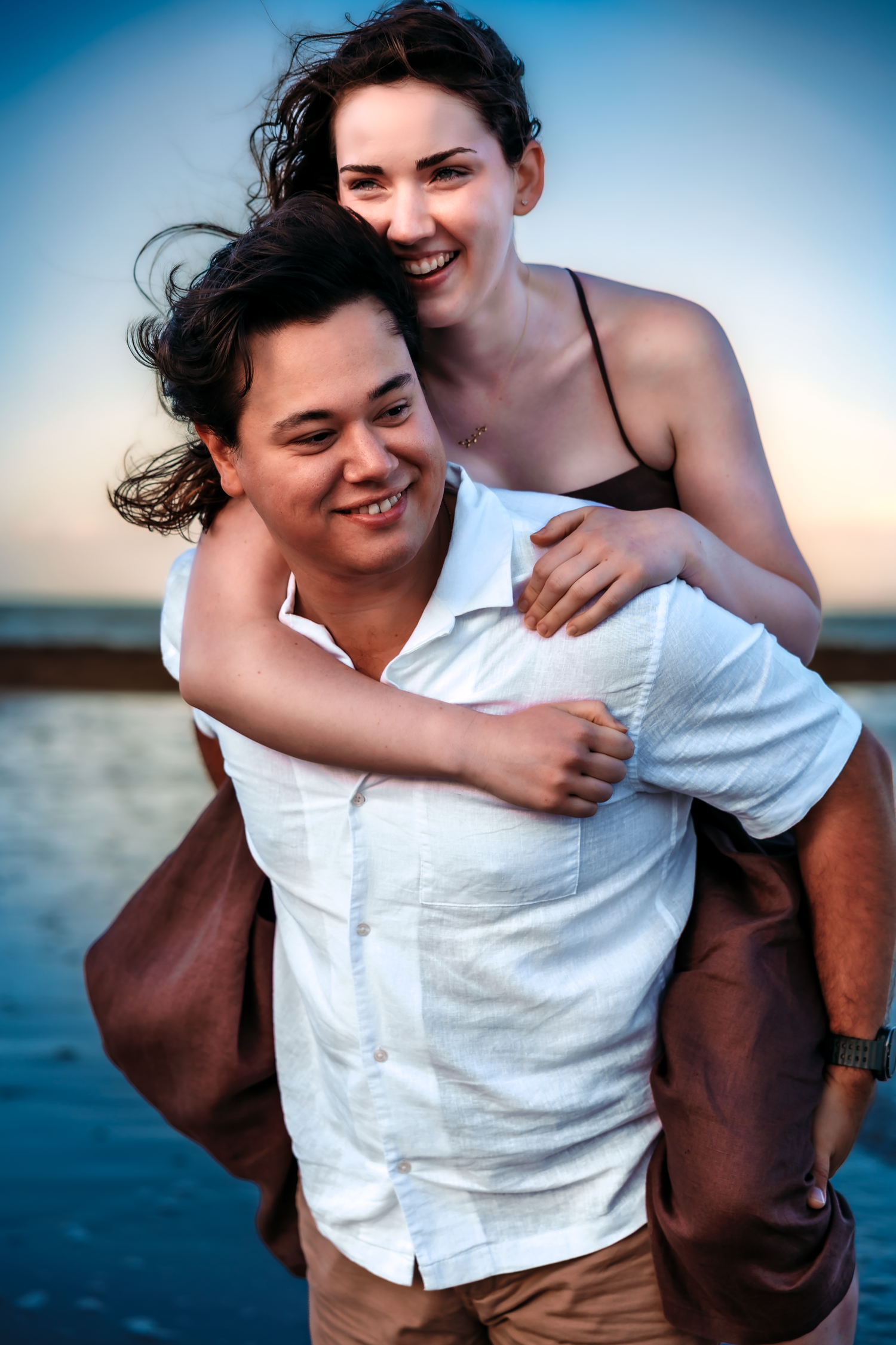 Happy couple sharing a piggyback ride on the beach at sunset, smiling and embracing near the ocean.