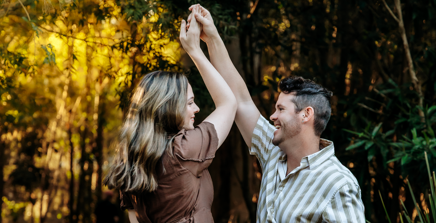 A happy couple dances together outdoors surrounded by lush golden autumn foliage.
