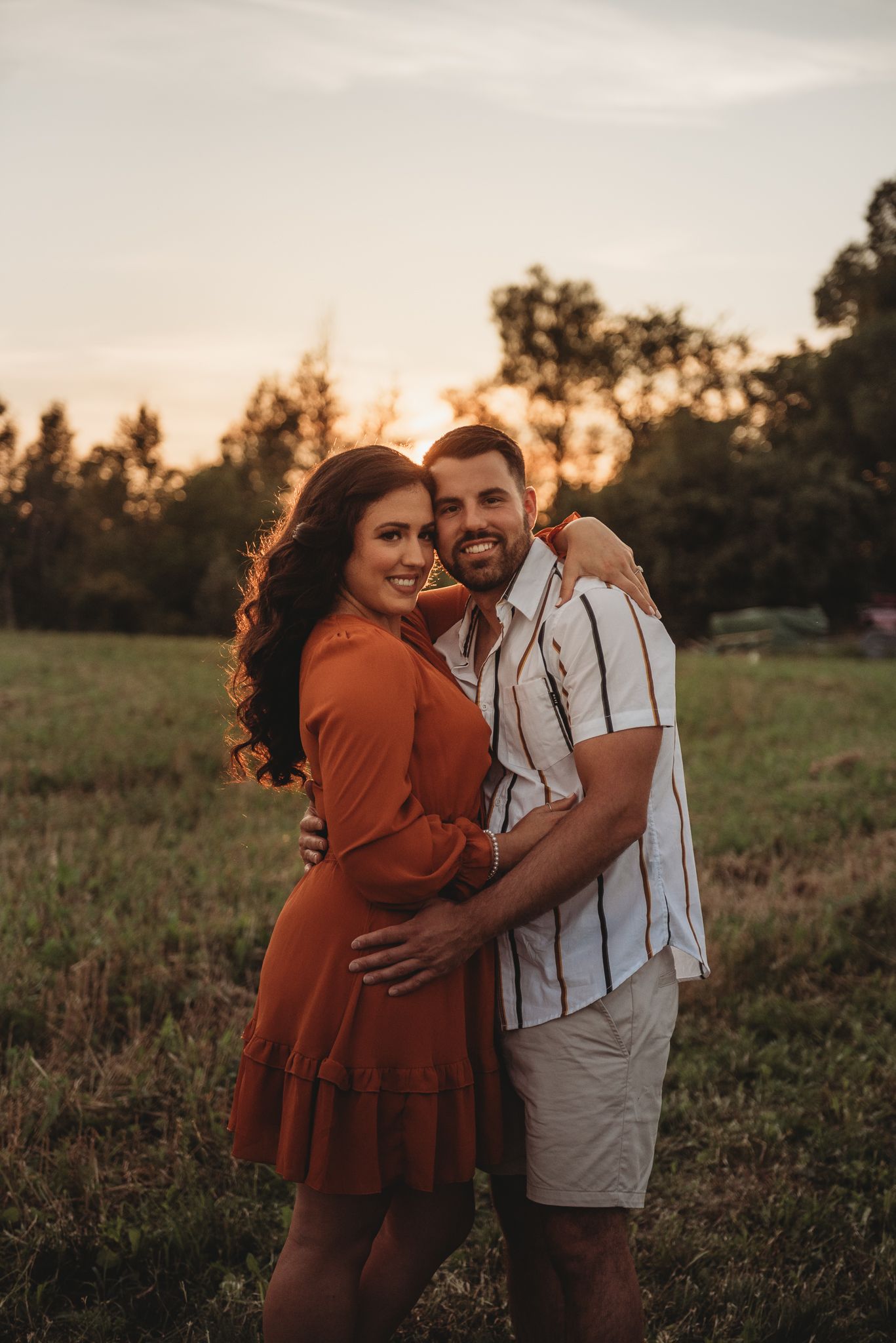 Couple embraces and laughs together in a golden sunlit field during sunset.
