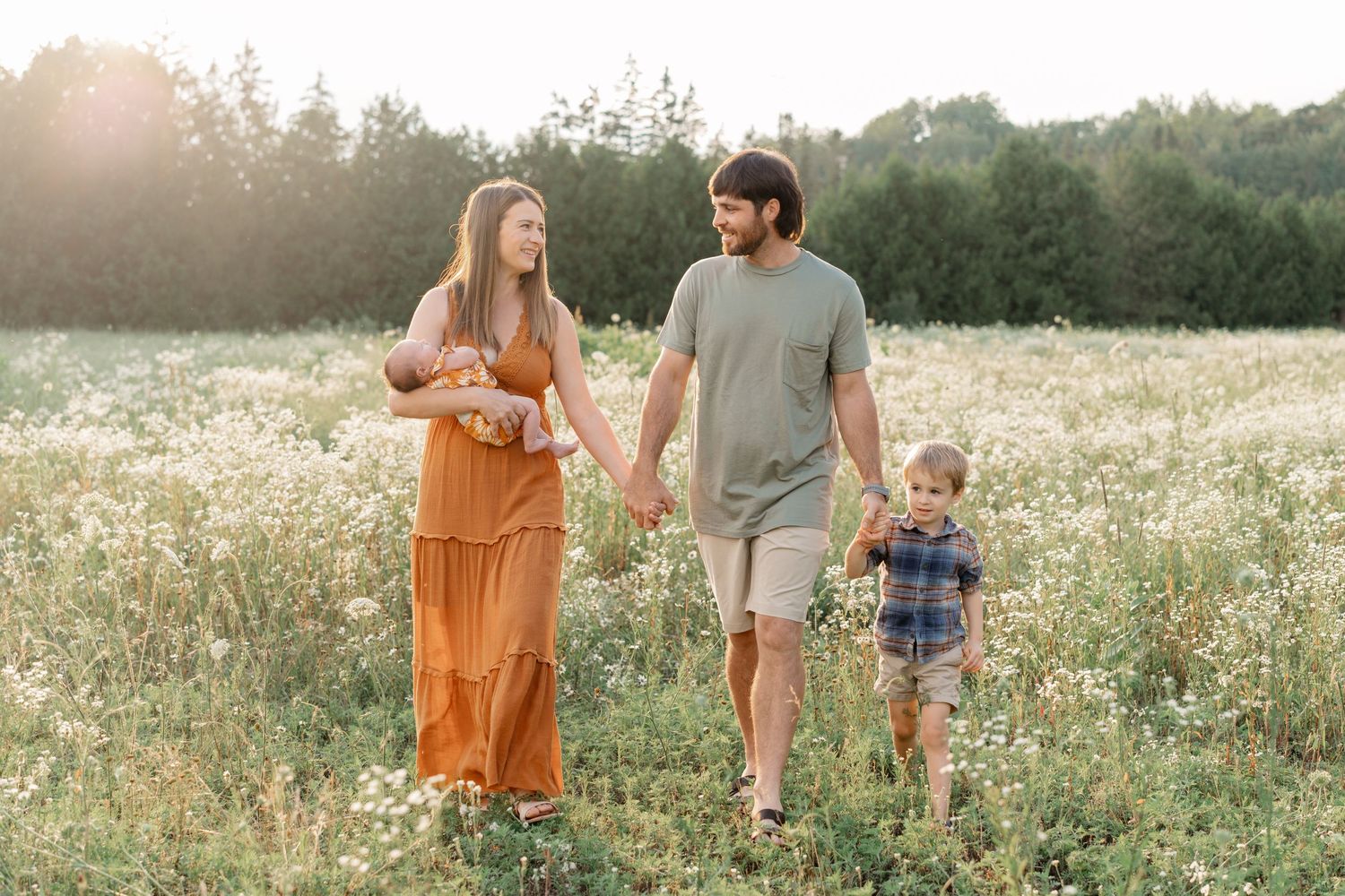 Couple strolls through a sunlit meadow with their child during a warm afternoon.