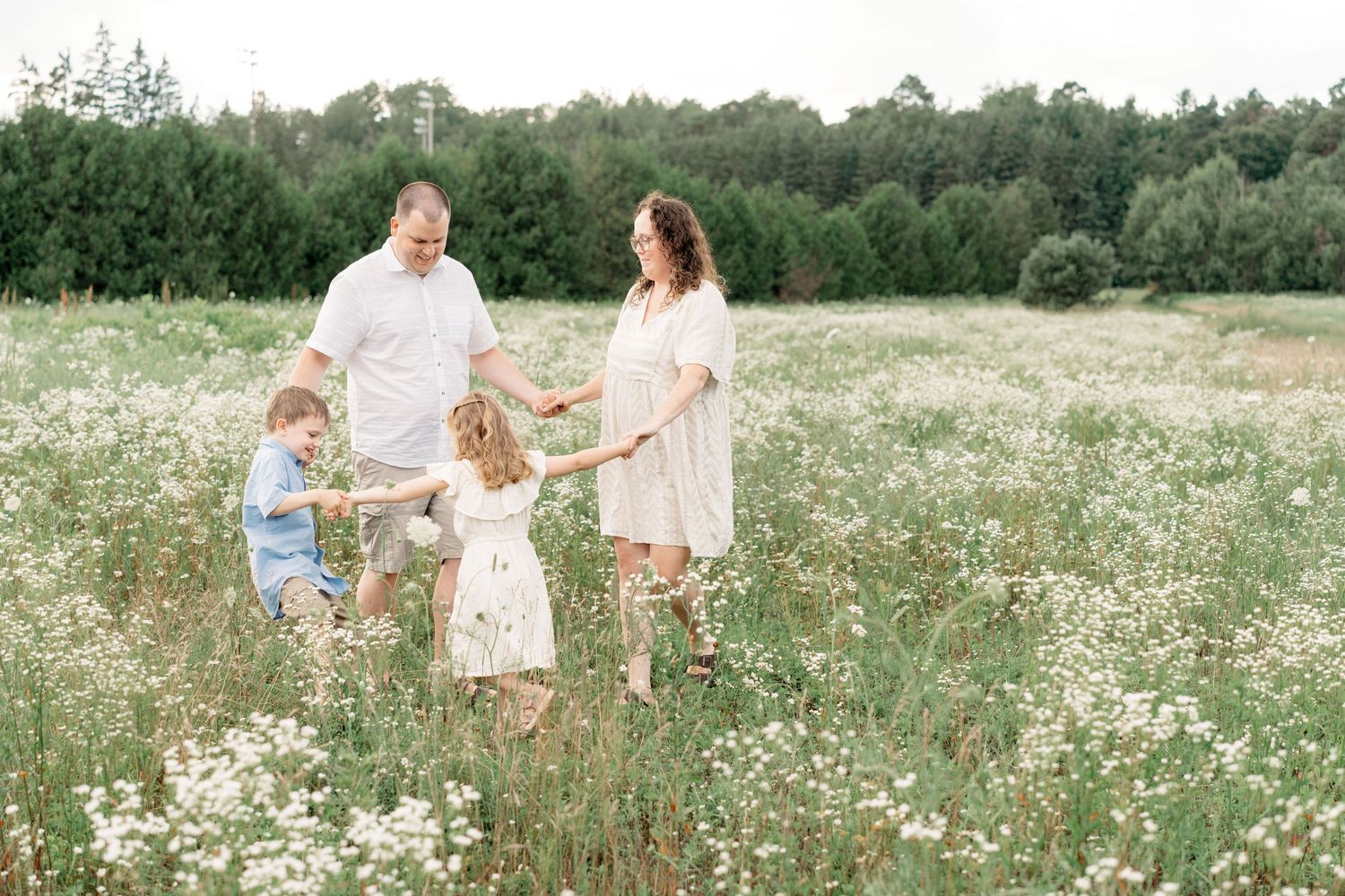 A family holds hands while standing together in a wildflower meadow on a sunny summer day.