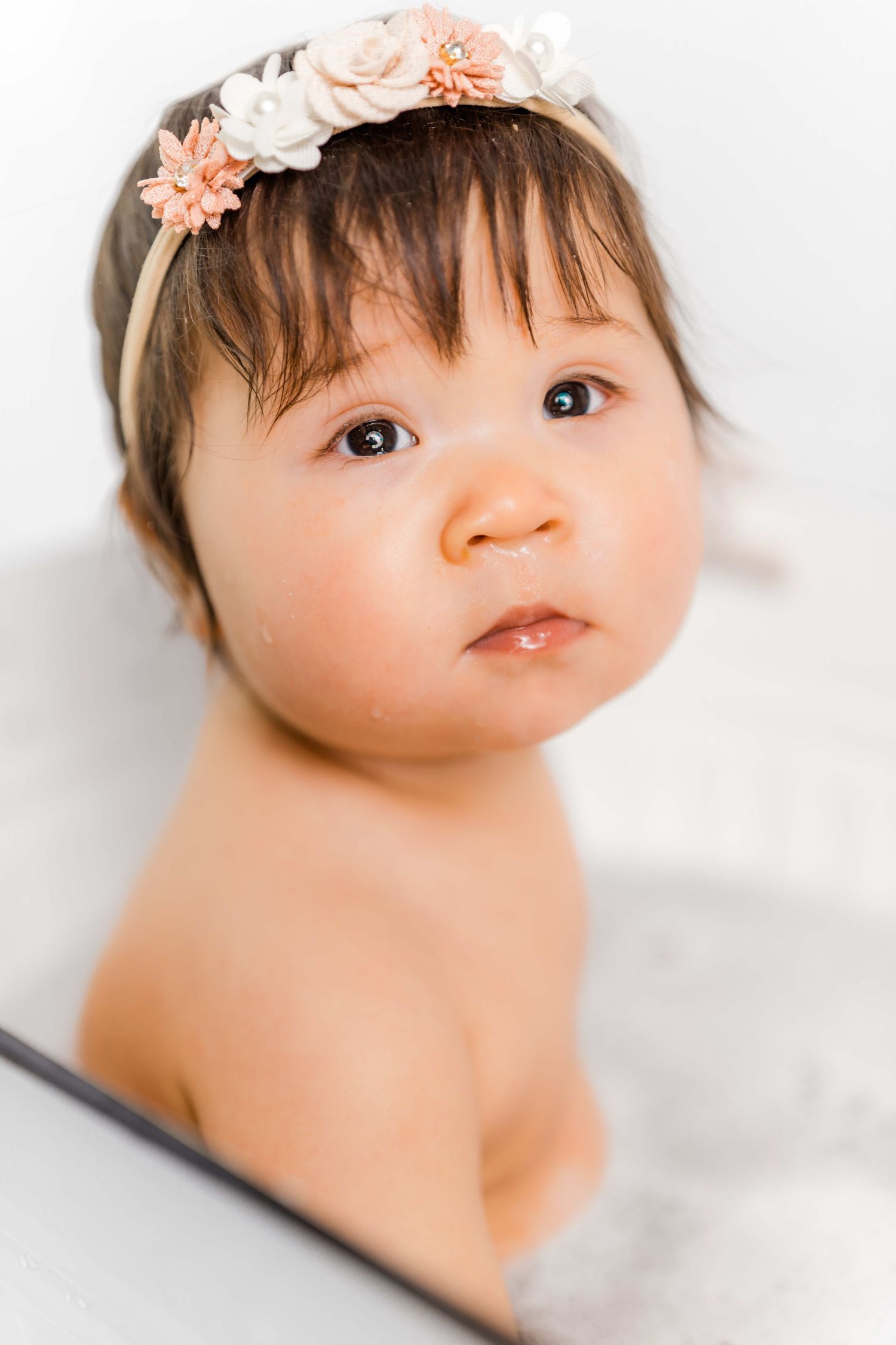 A baby wearing delicate floral headbands looks upward in a series of gentle portrait poses against a white background.