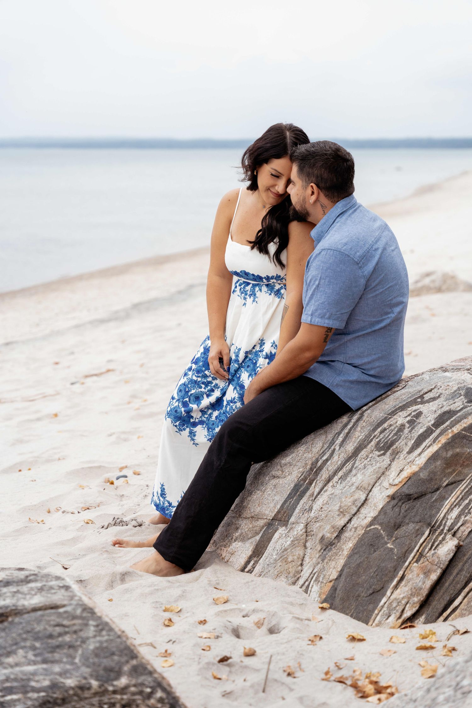 A couple sits together on a large driftwood log at the beach during a romantic photoshoot session.