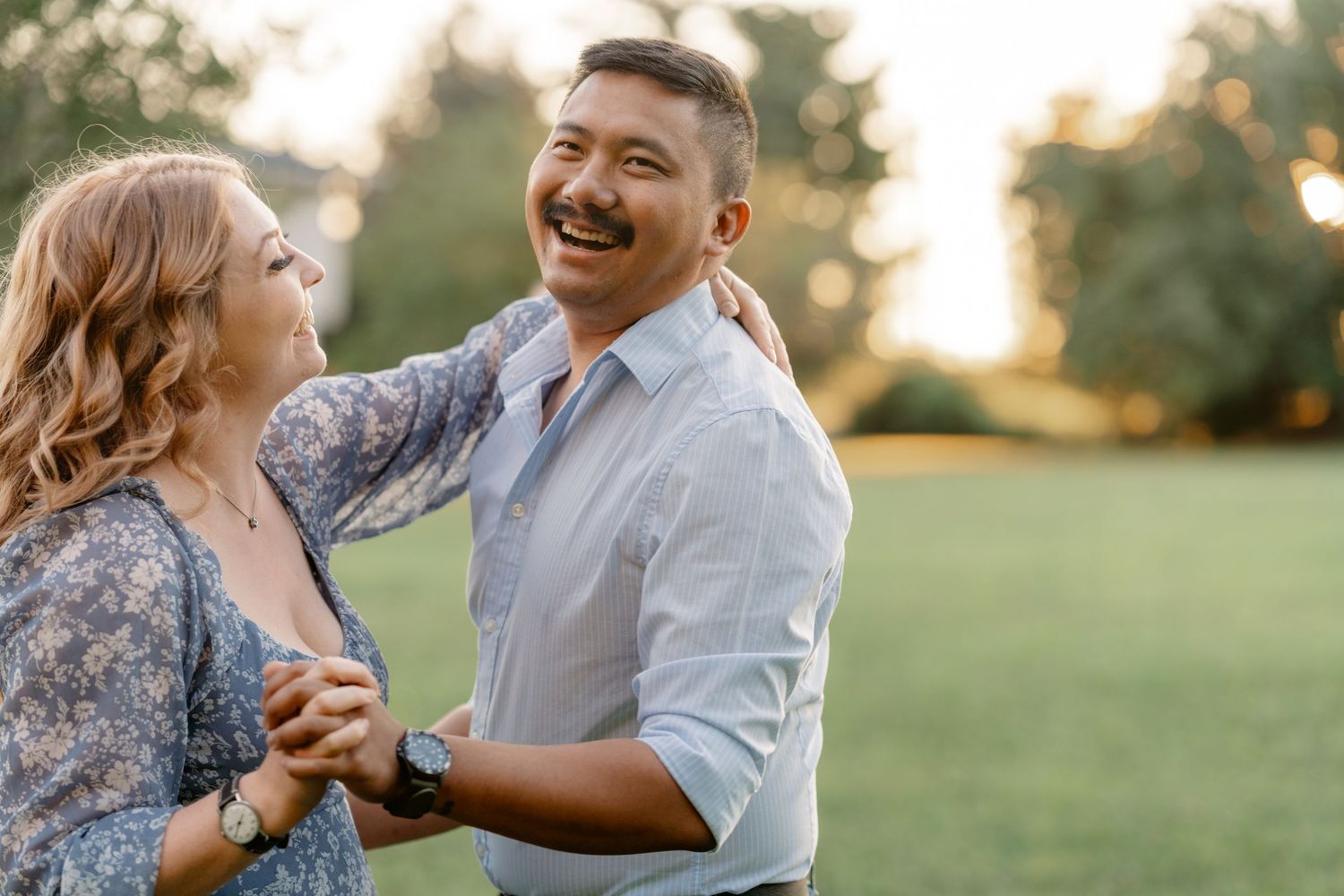 A couple dances together in a sunlit meadow during golden hour, creating a romantic outdoor moment.