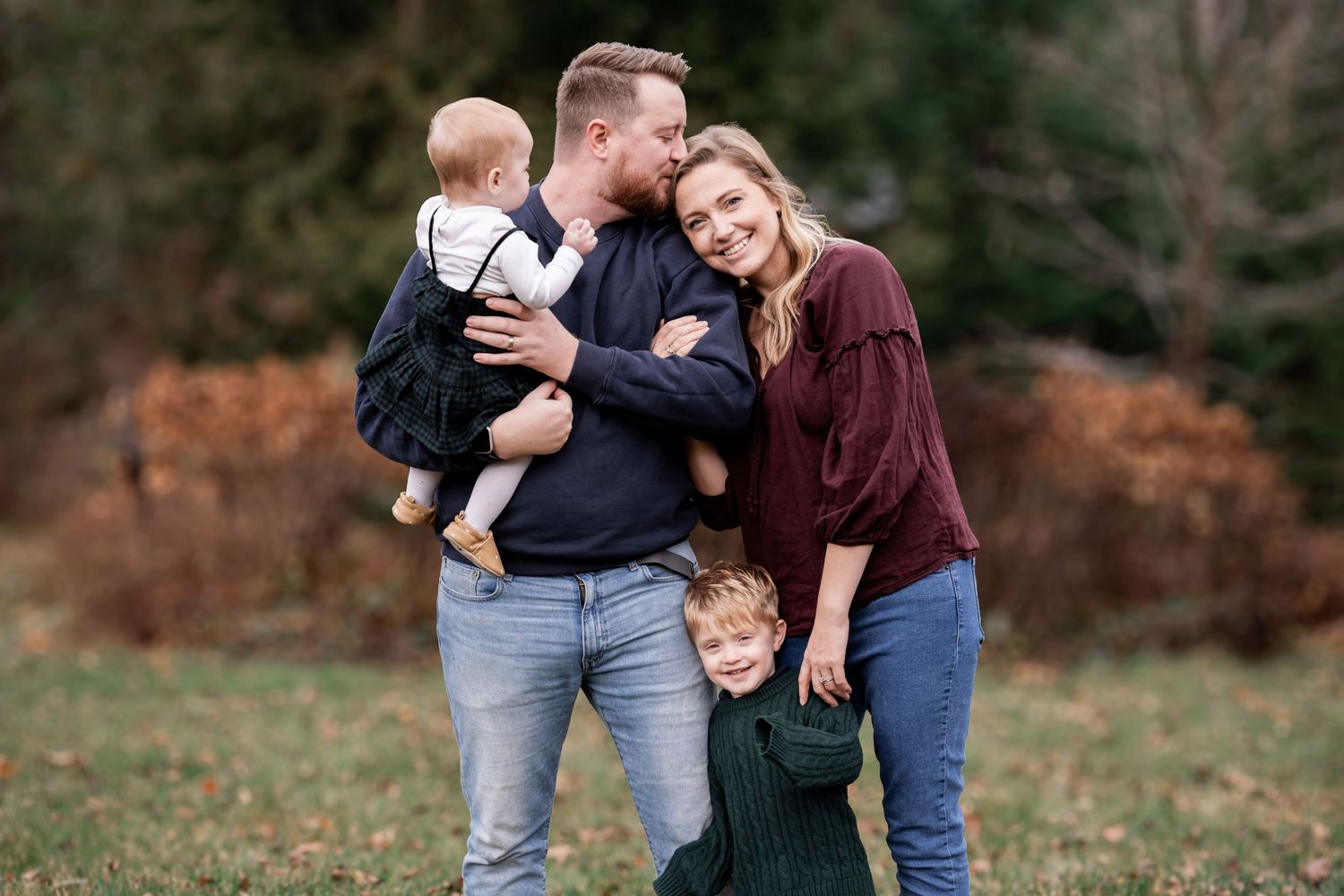 A family group shares tender moments together during an outdoor autumn photoshoot in a park setting.