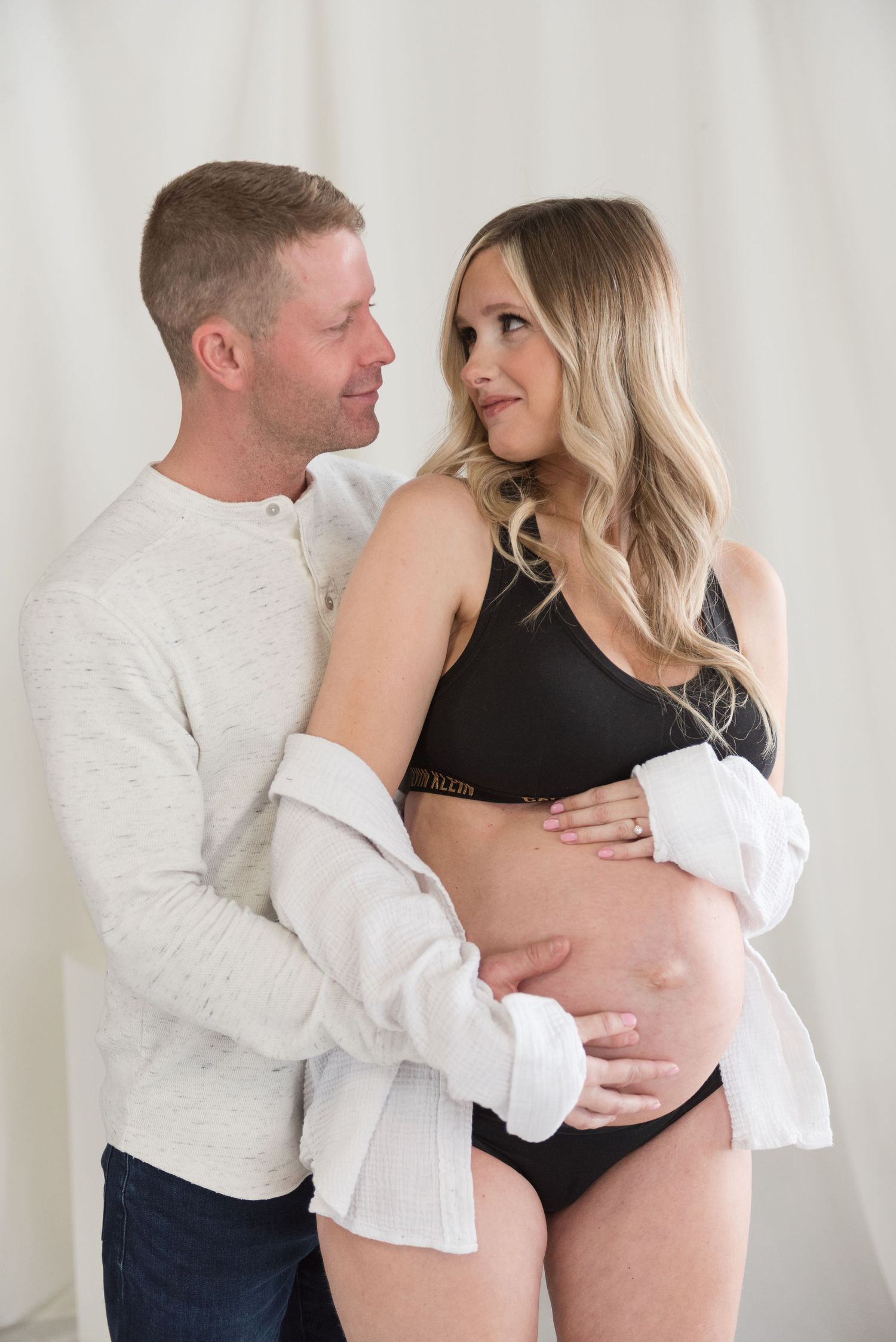 A couple in white and black clothing embraces lovingly against a light background in a series of intimate photos.