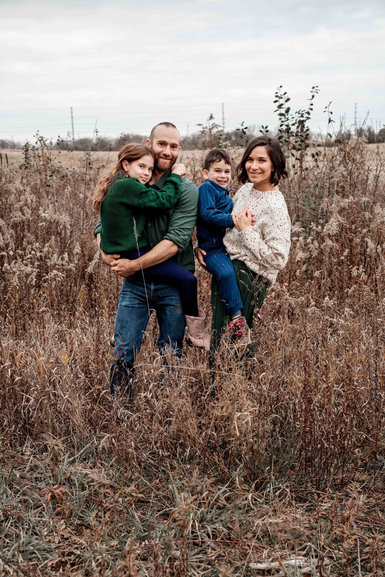 A family poses together in a rustic field with dried grasses during an outdoor photo session.