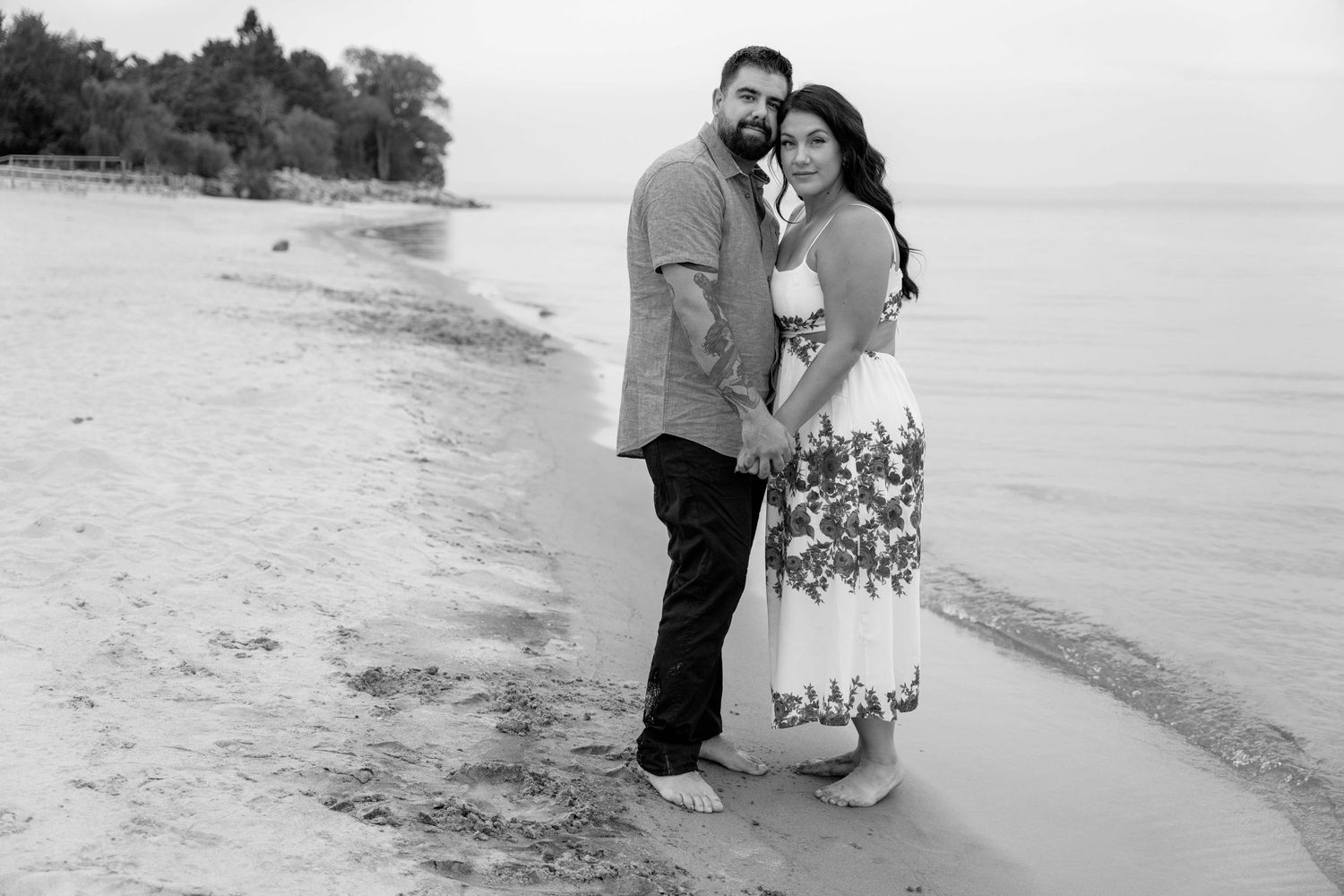 A couple embraces on a peaceful beach shoreline in black and white photography.