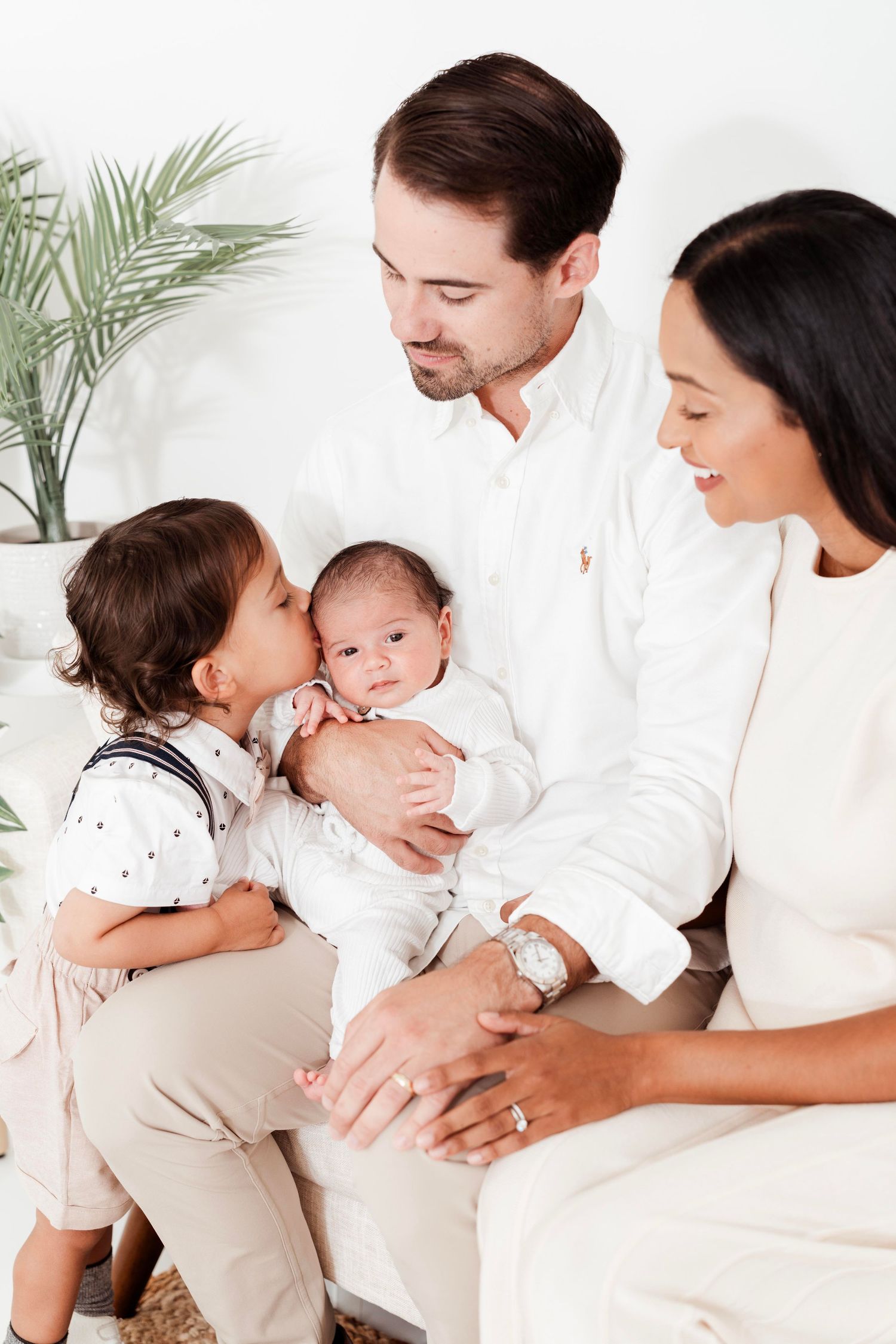 A loving family in white clothing shares tender moments with their newborn baby in a series of connected portraits.