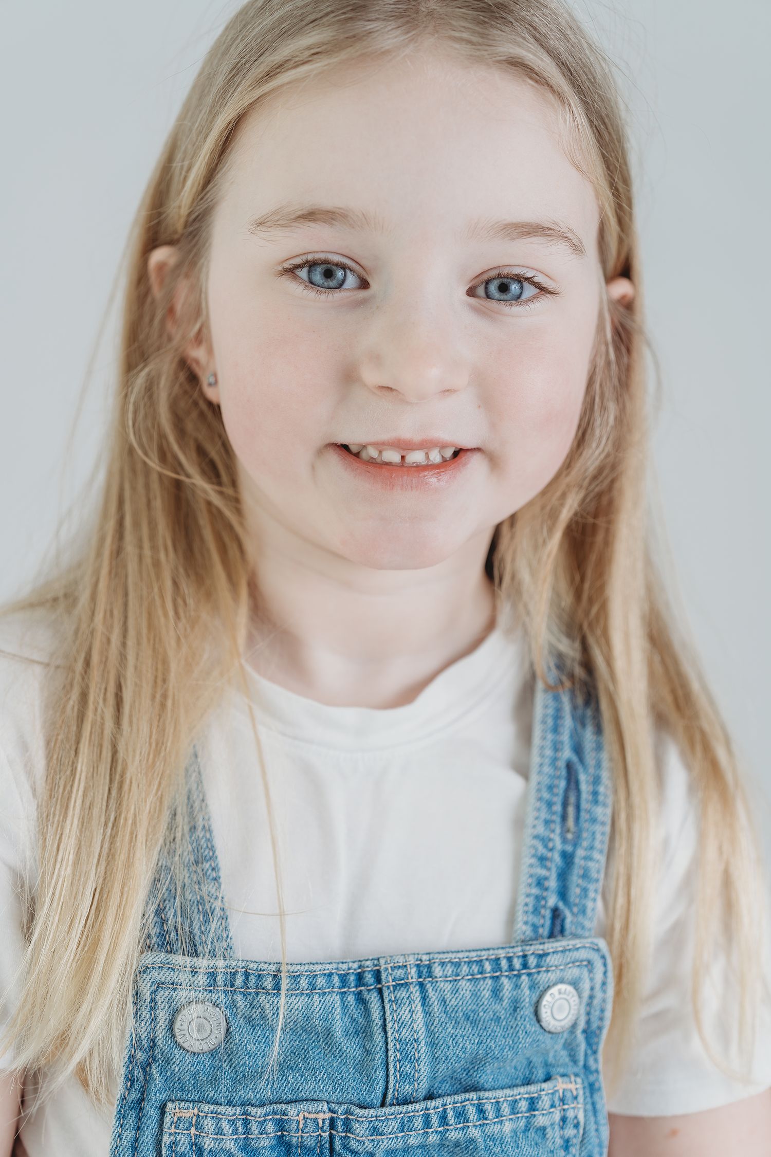 A series of four candid portraits showing a young child in denim overalls and white shirt against a light background.