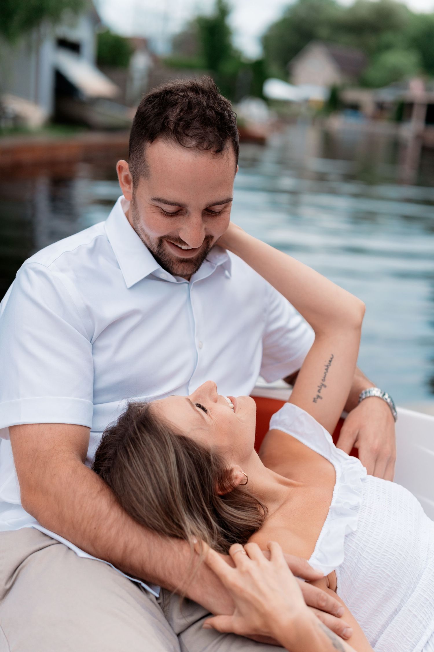 A romantic couple in white outfits share an intimate moment while relaxing together by the water.