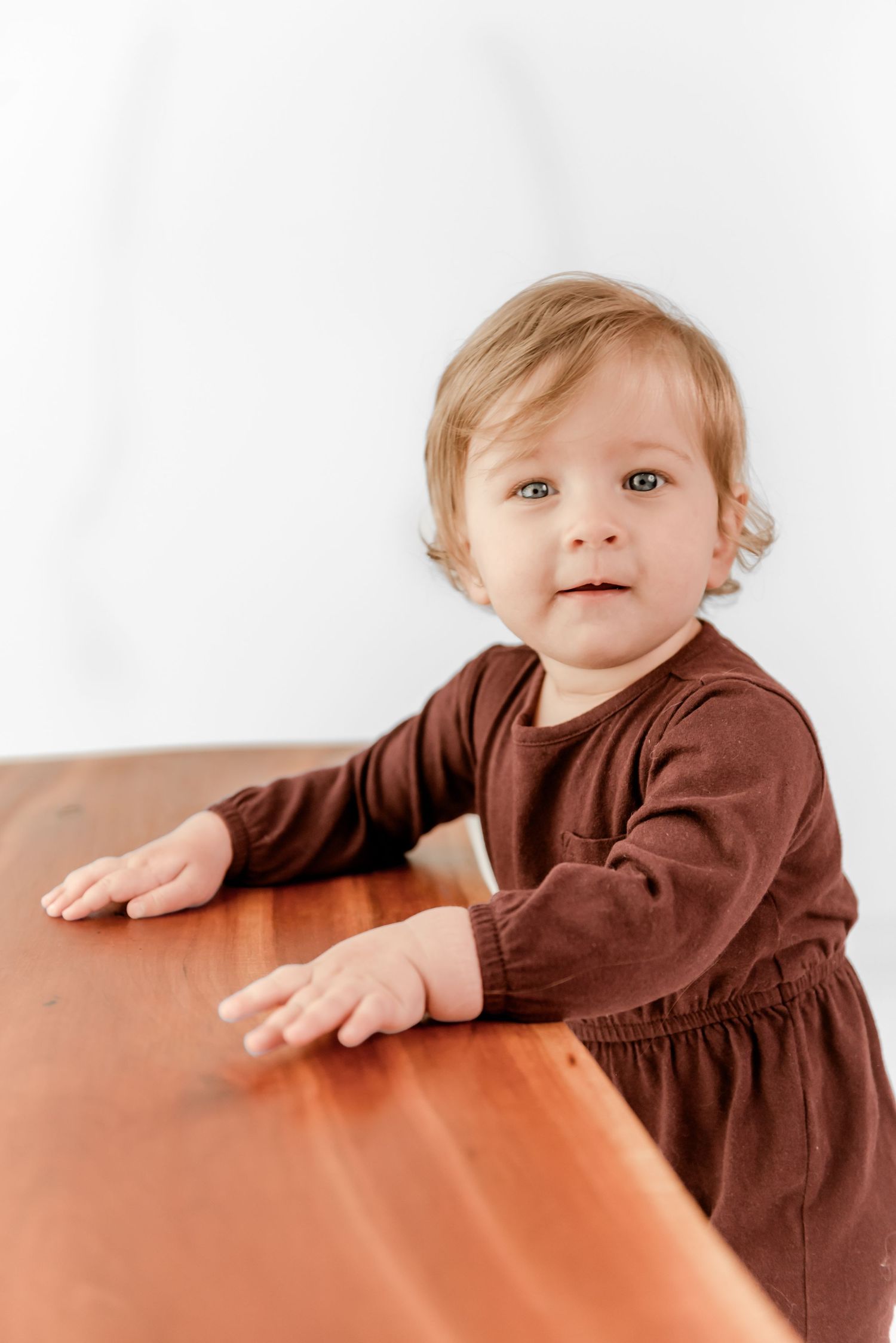 A toddler in a brown long-sleeve shirt peeks over an orange surface in a series of playful poses.
