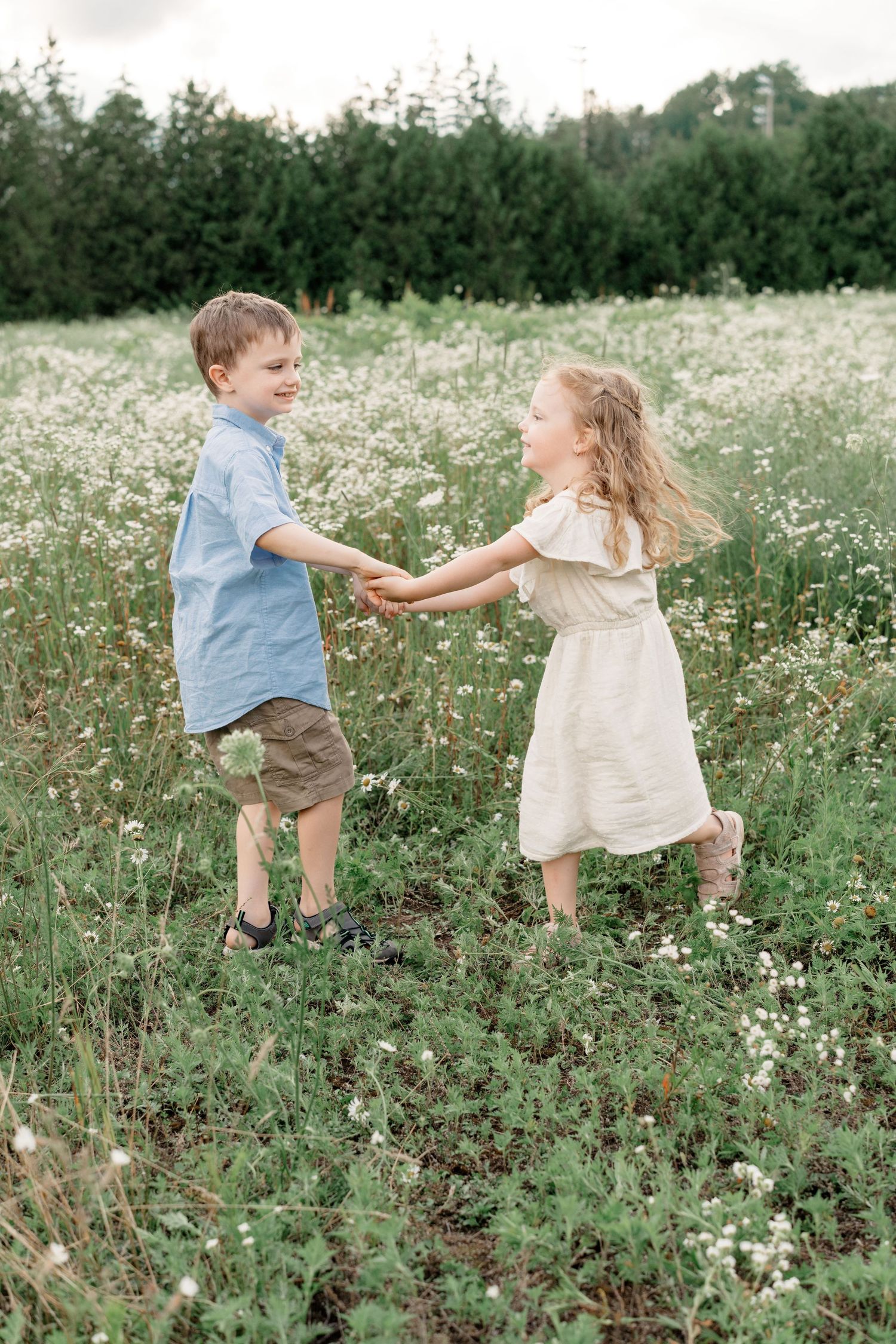 Two young children play and dance together in a blooming wildflower meadow on a summer day.