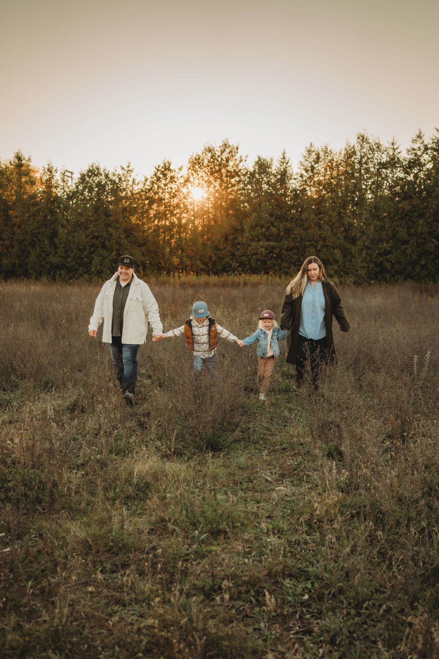 A family walks hand in hand through a golden field at sunset with trees silhouetted in the background.