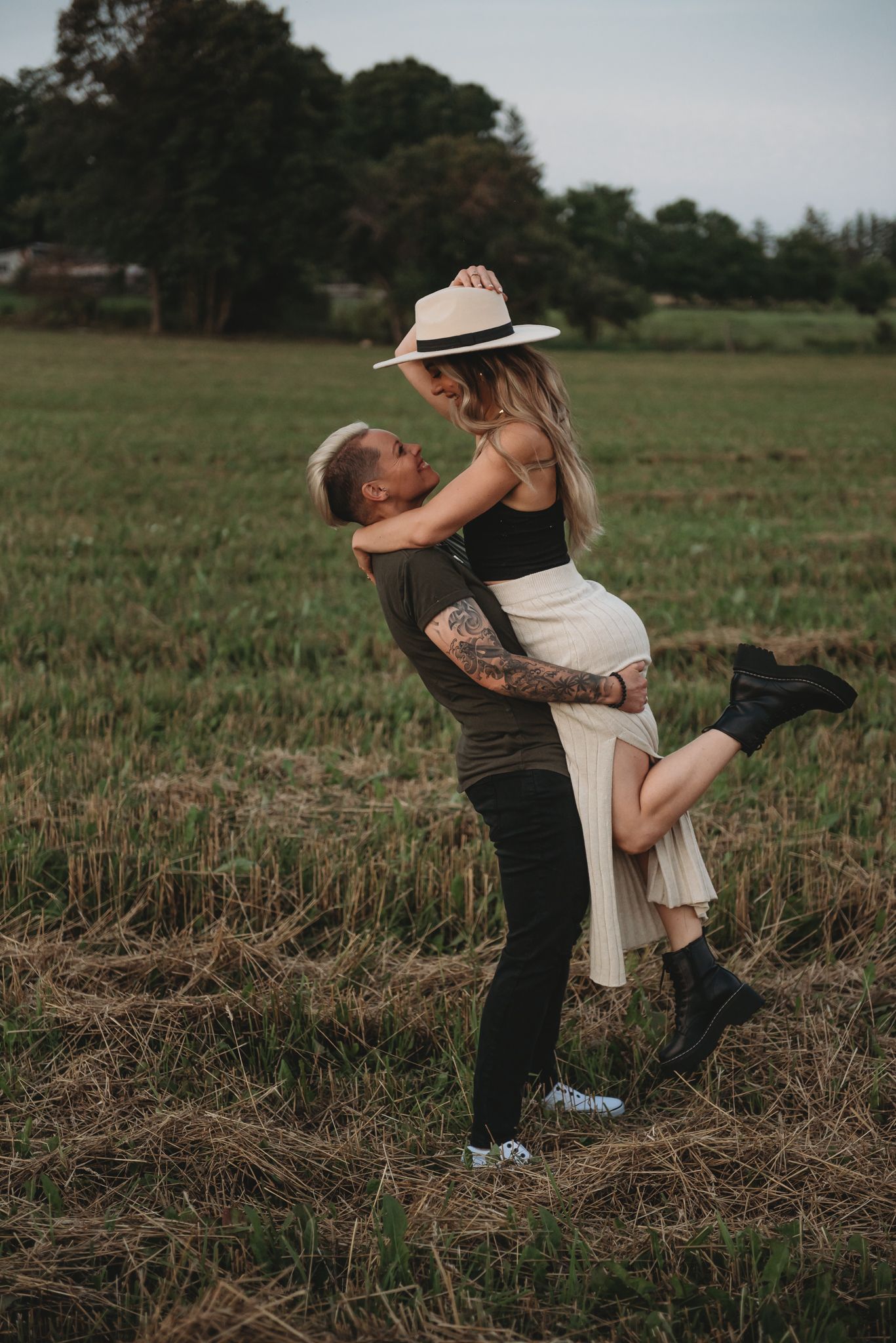 A couple shares an intimate dance in a rustic field at sunset, creating a romantic outdoor moment.