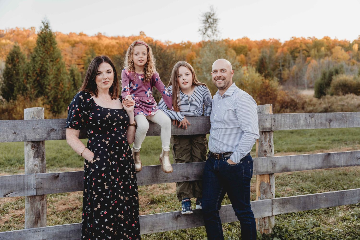 Group enjoying an autumn photoshoot by a rustic wooden fence with colorful fall foliage in the background.