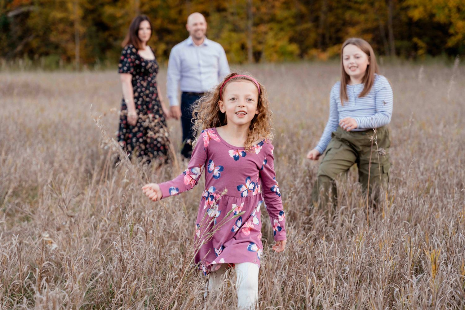 Family enjoying a candid moment together in a golden autumn field during sunset.