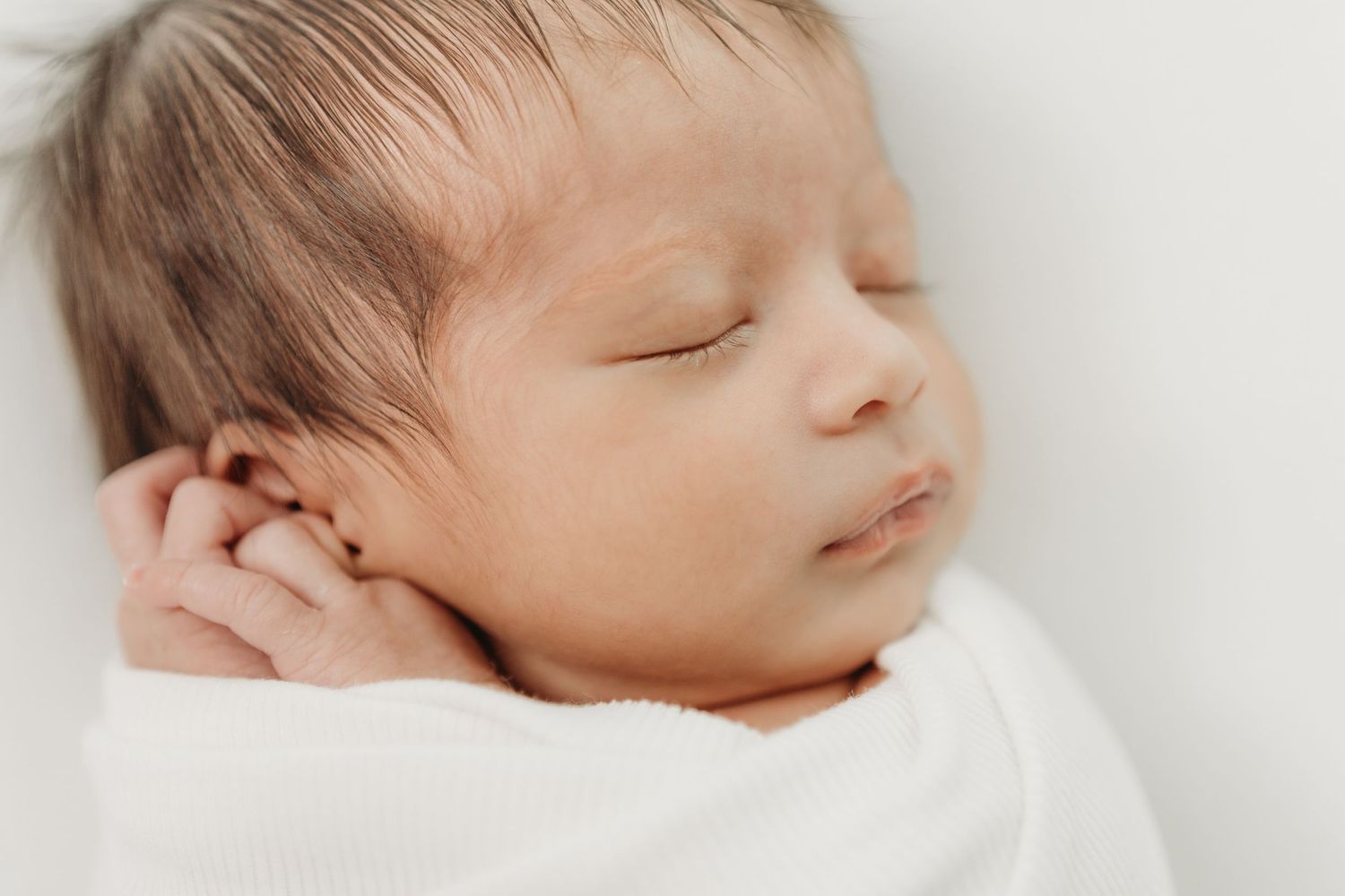 Newborn baby sleeping peacefully in soft white bedding.