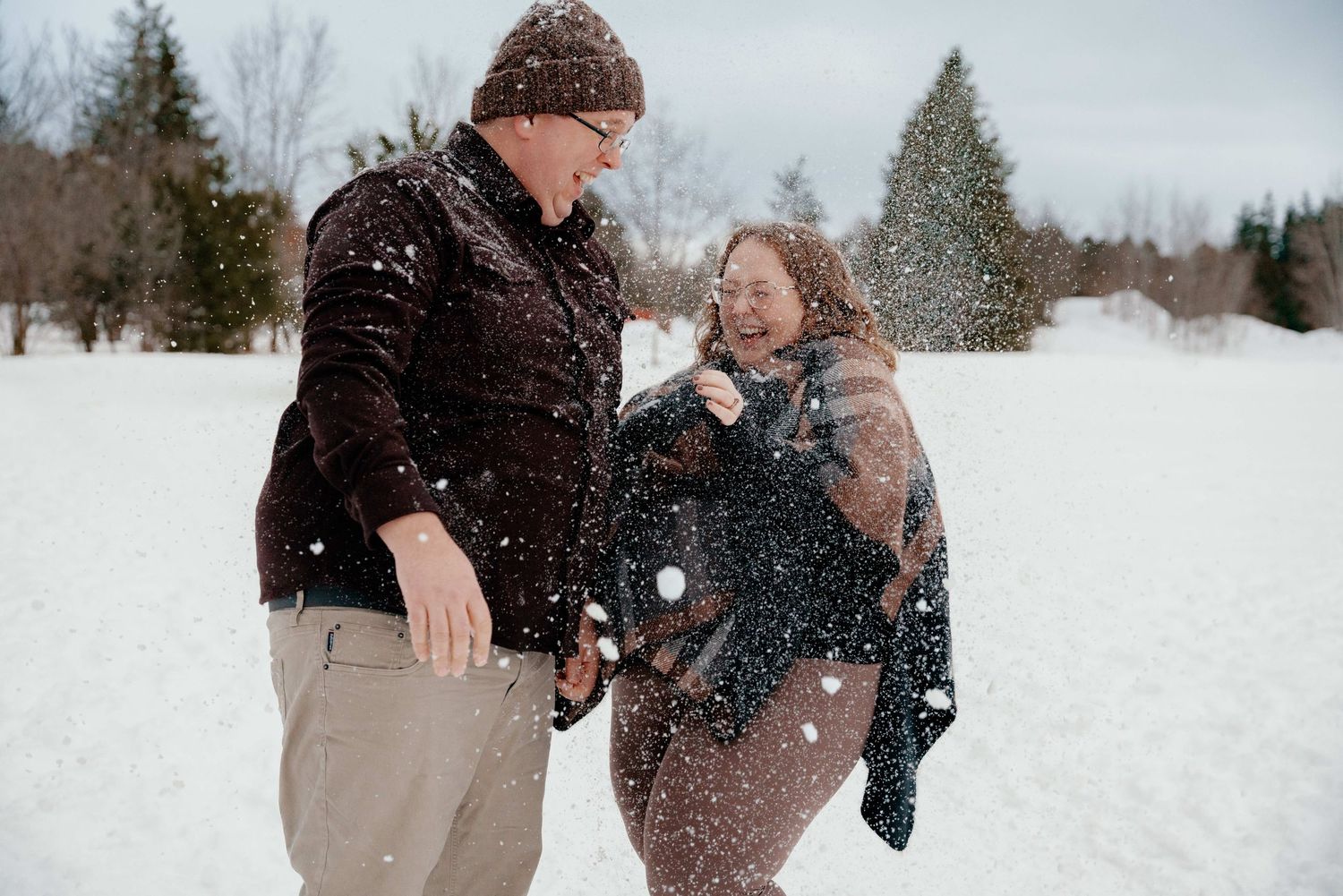 A couple shares a joyful moment together in a snowy winter landscape during falling snow.