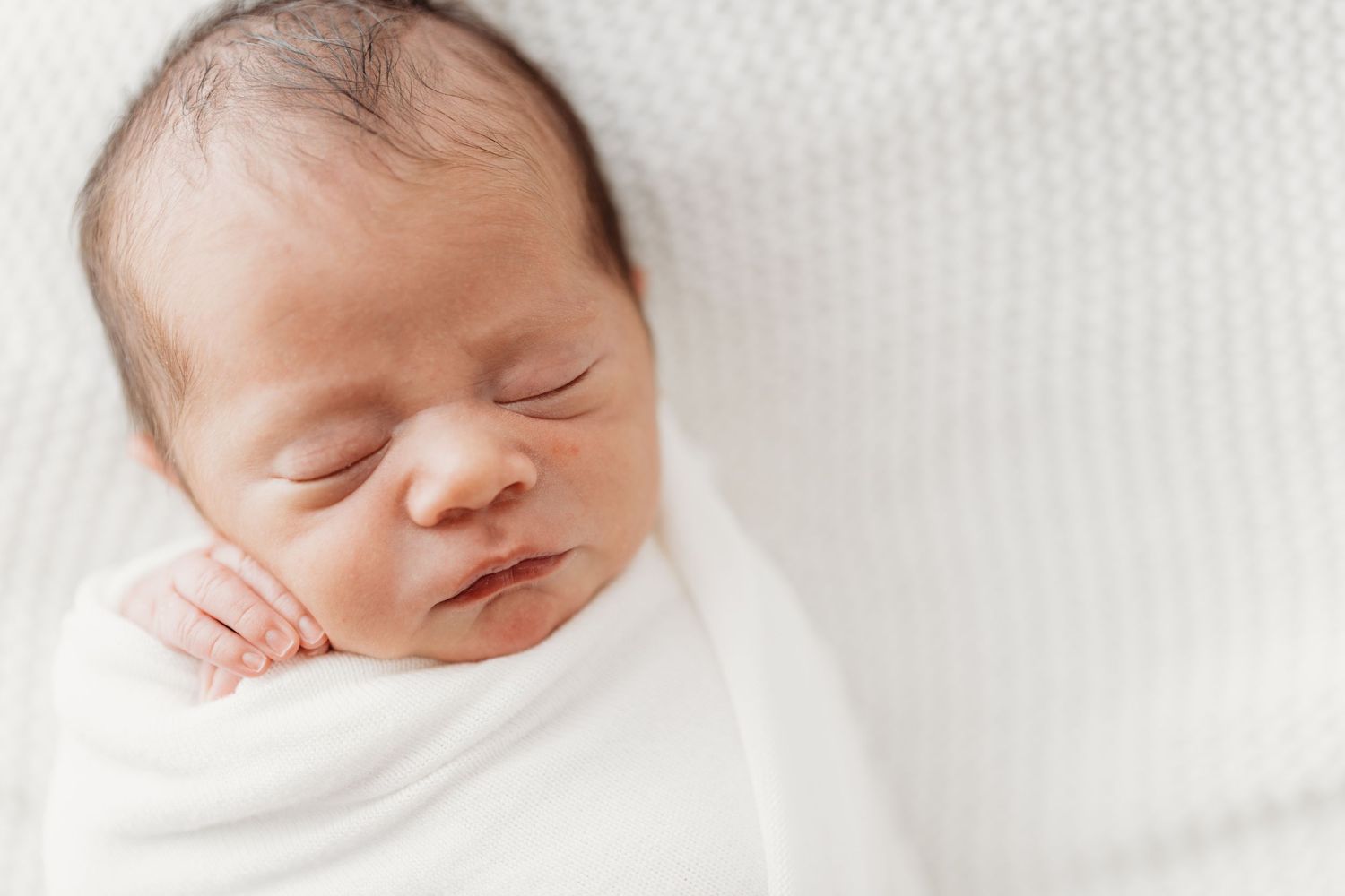 Serene newborn baby sleeping peacefully wrapped in white swaddle blanket.