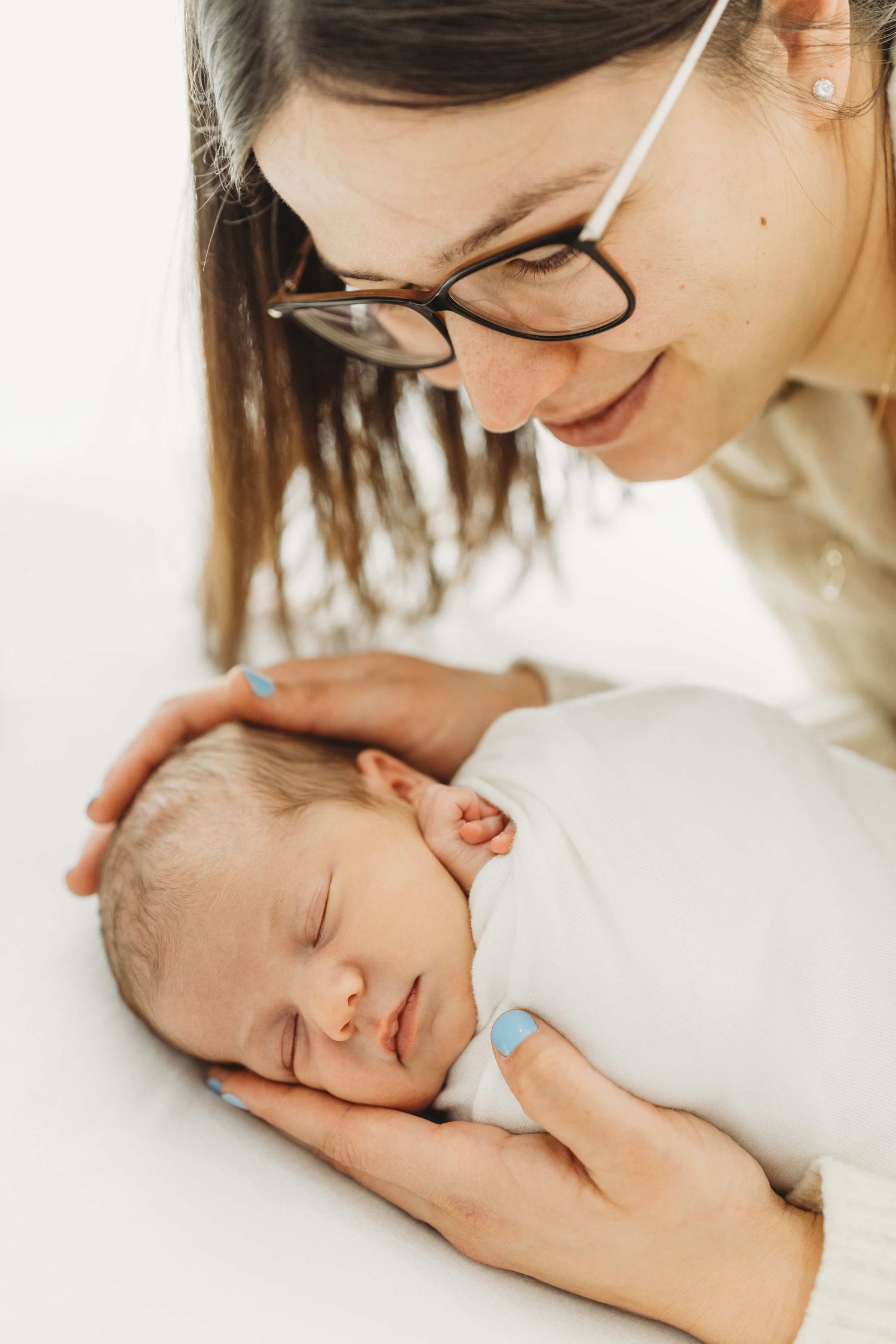 A tender moment between parent and sleeping newborn baby in soft white lighting.
