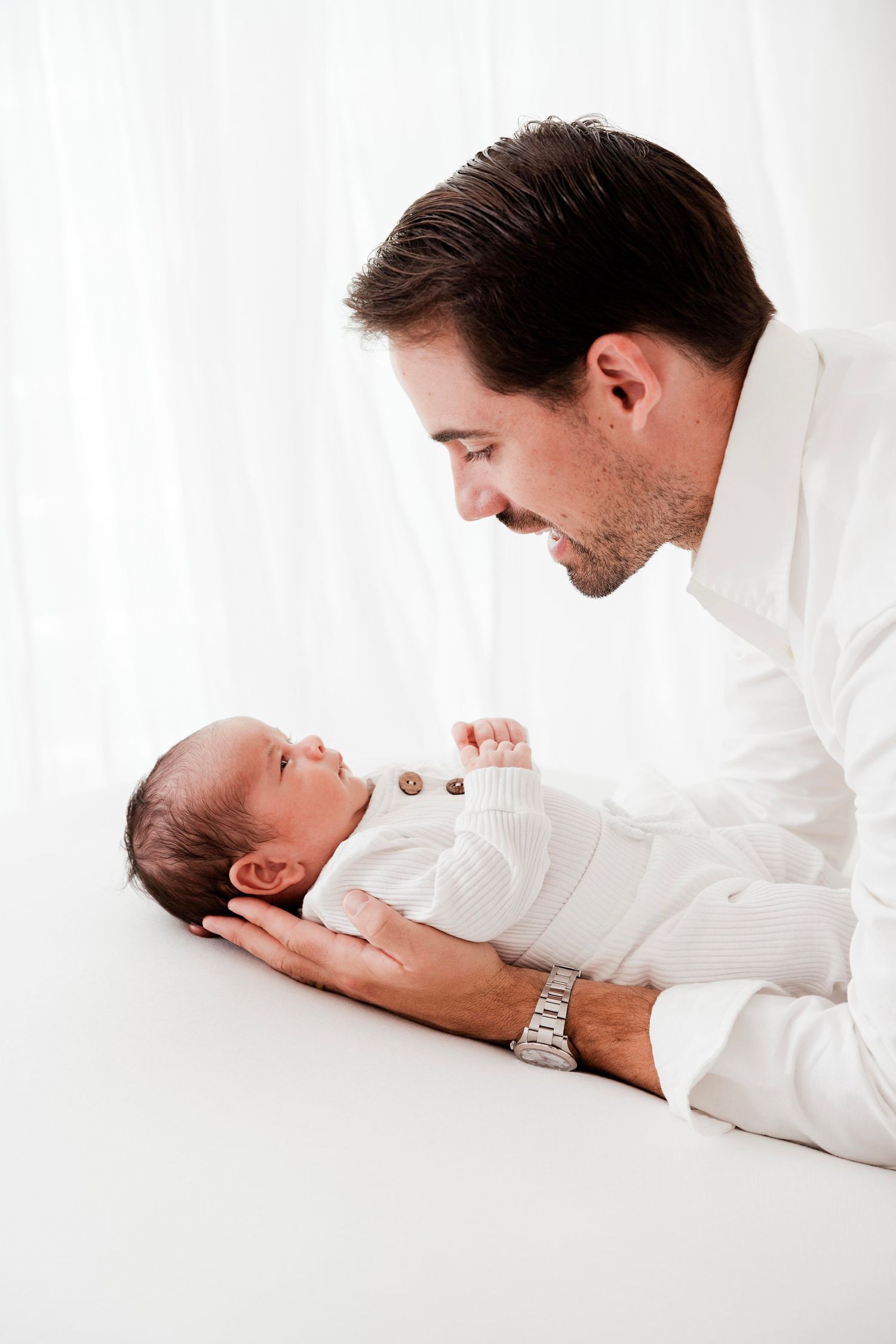 A tender moment between parent and newborn baby in white, showing three progressive angles of gentle interaction.