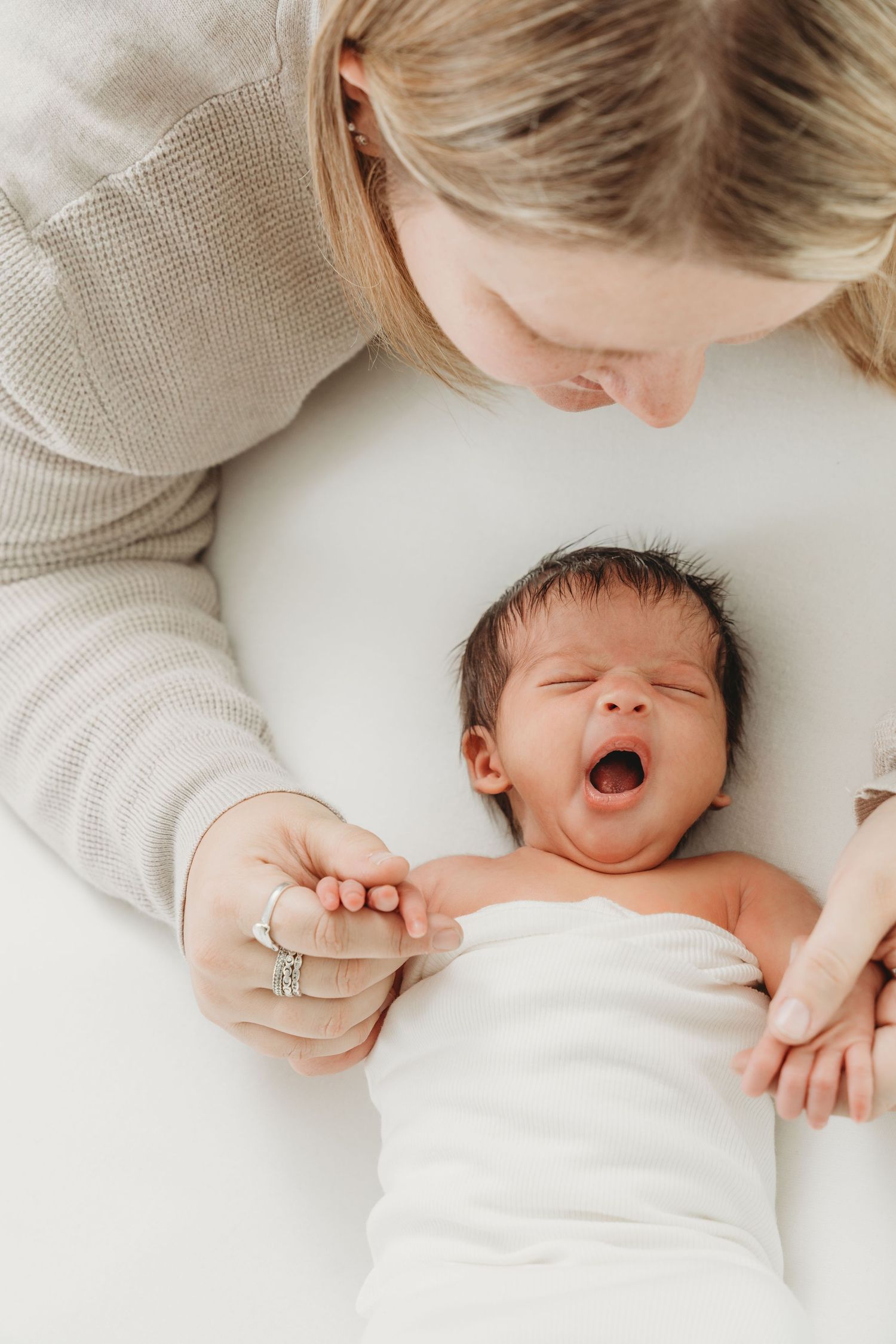 A sequence of tender moments showing a newborn baby yawning while lying on white bedding.