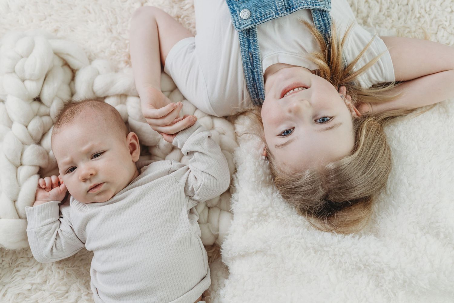 Two people lying on a soft white carpet, wearing light colored clothing while relaxing together.