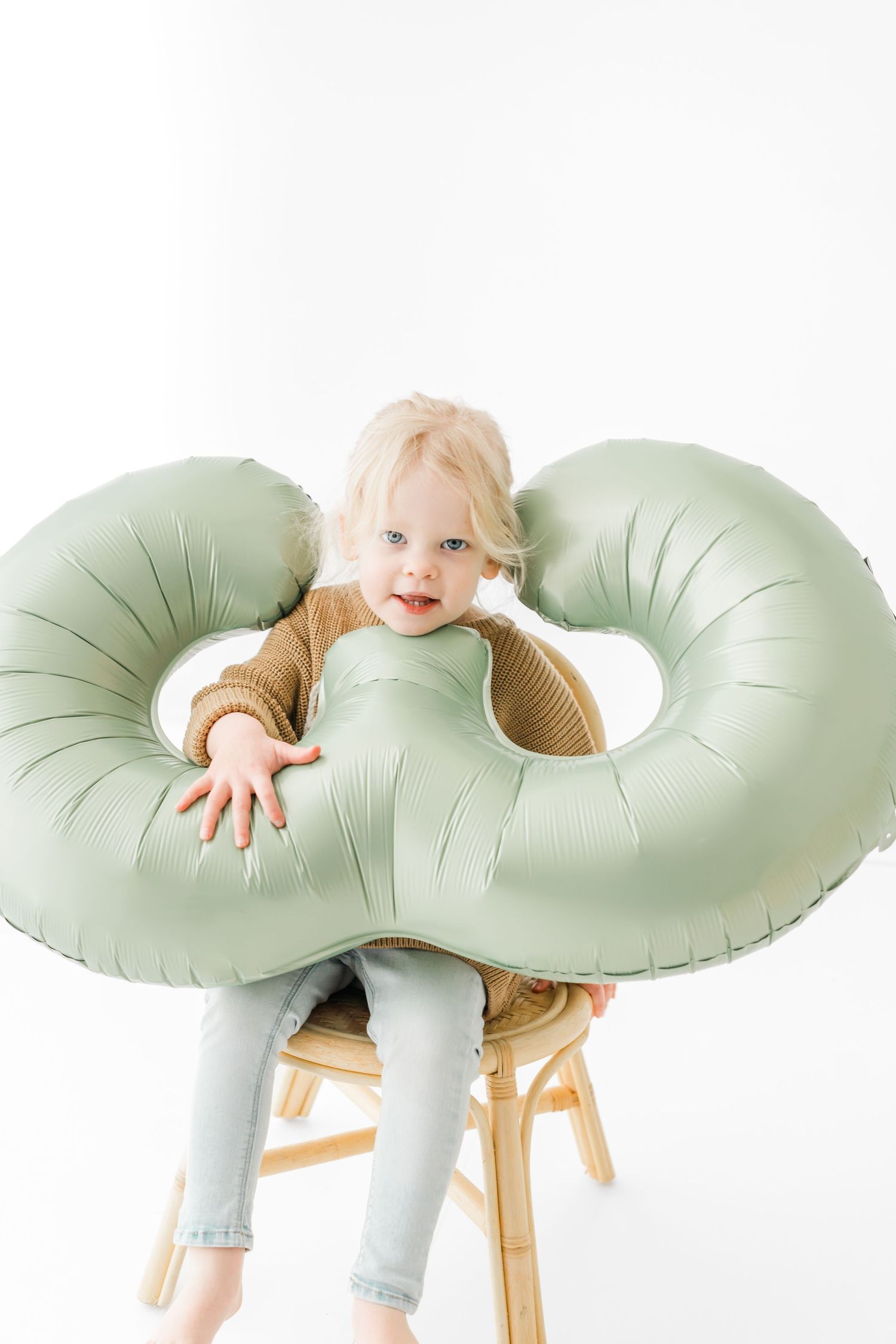Sequence of three photos showing a baby playing and peeking through a mint green donut-shaped pillow on a wooden chair.
