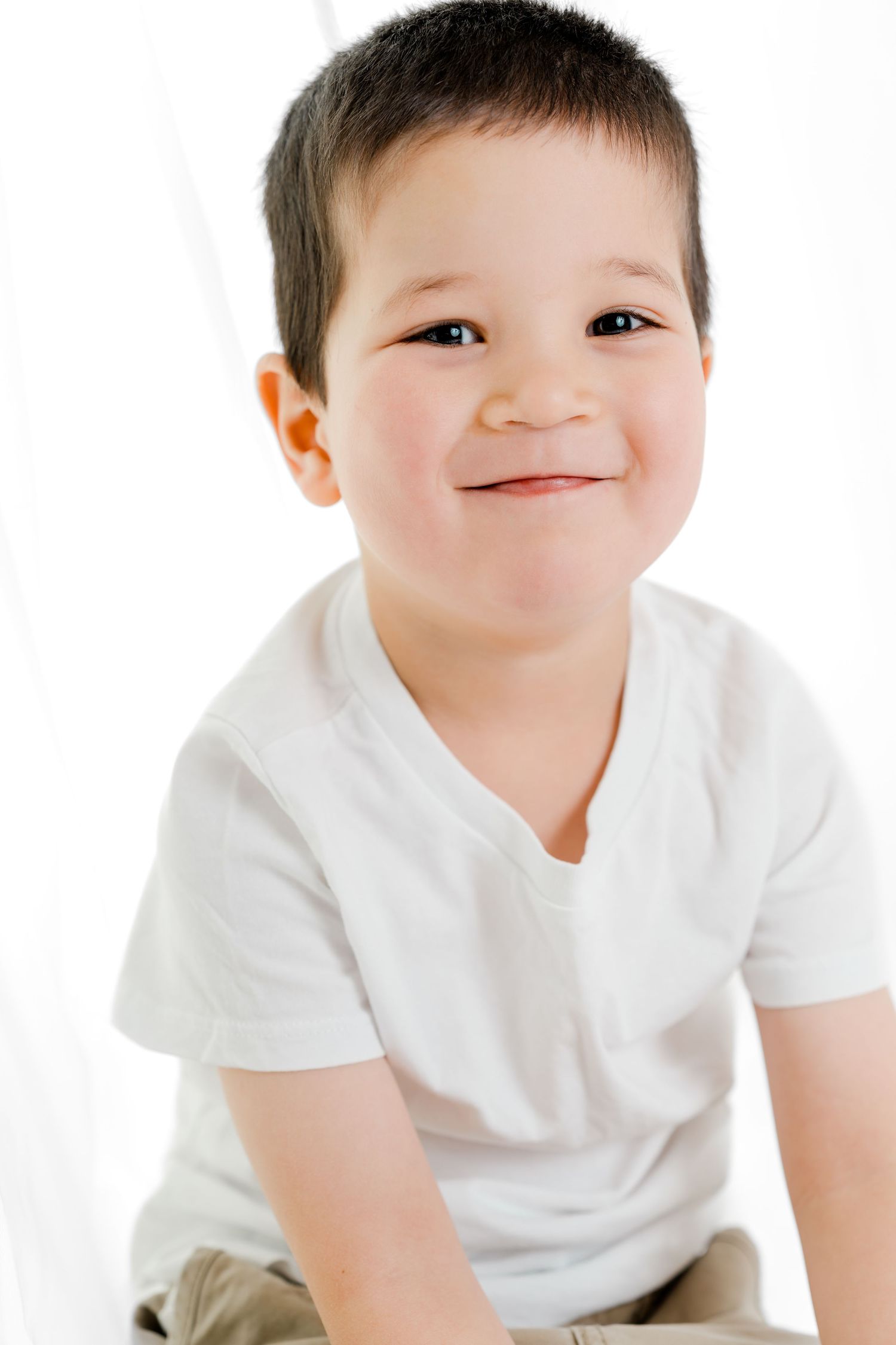 A young child in a white t-shirt crawls and smiles playfully on a white background.