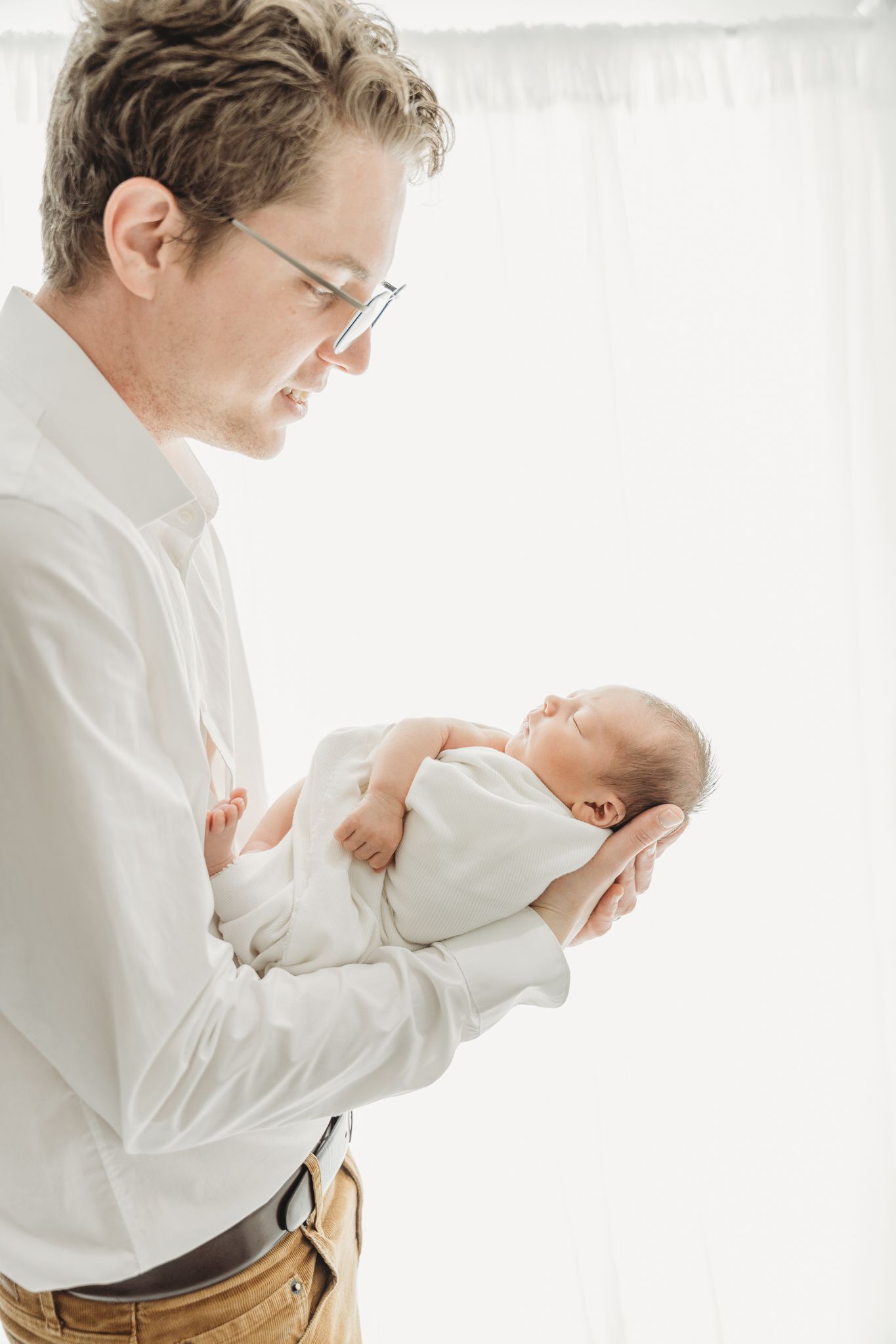 A series of four tender moments showing a parent in white shirt cradling and bonding with a newborn baby against white backdrop.