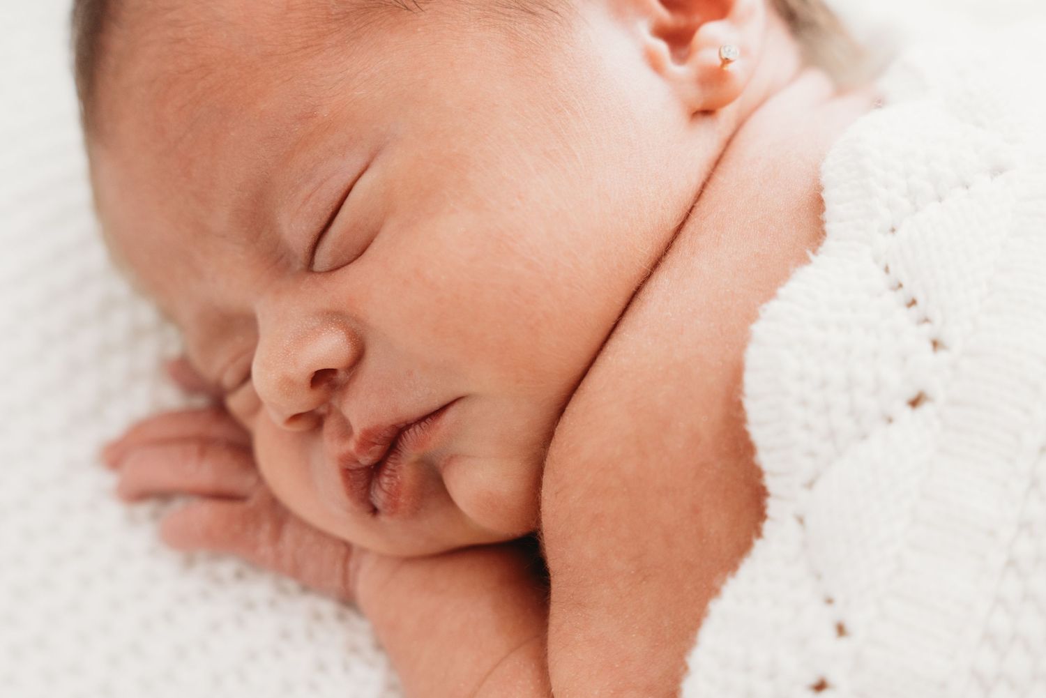 A sleeping newborn baby rests peacefully on soft white blankets in a close-up portrait.
