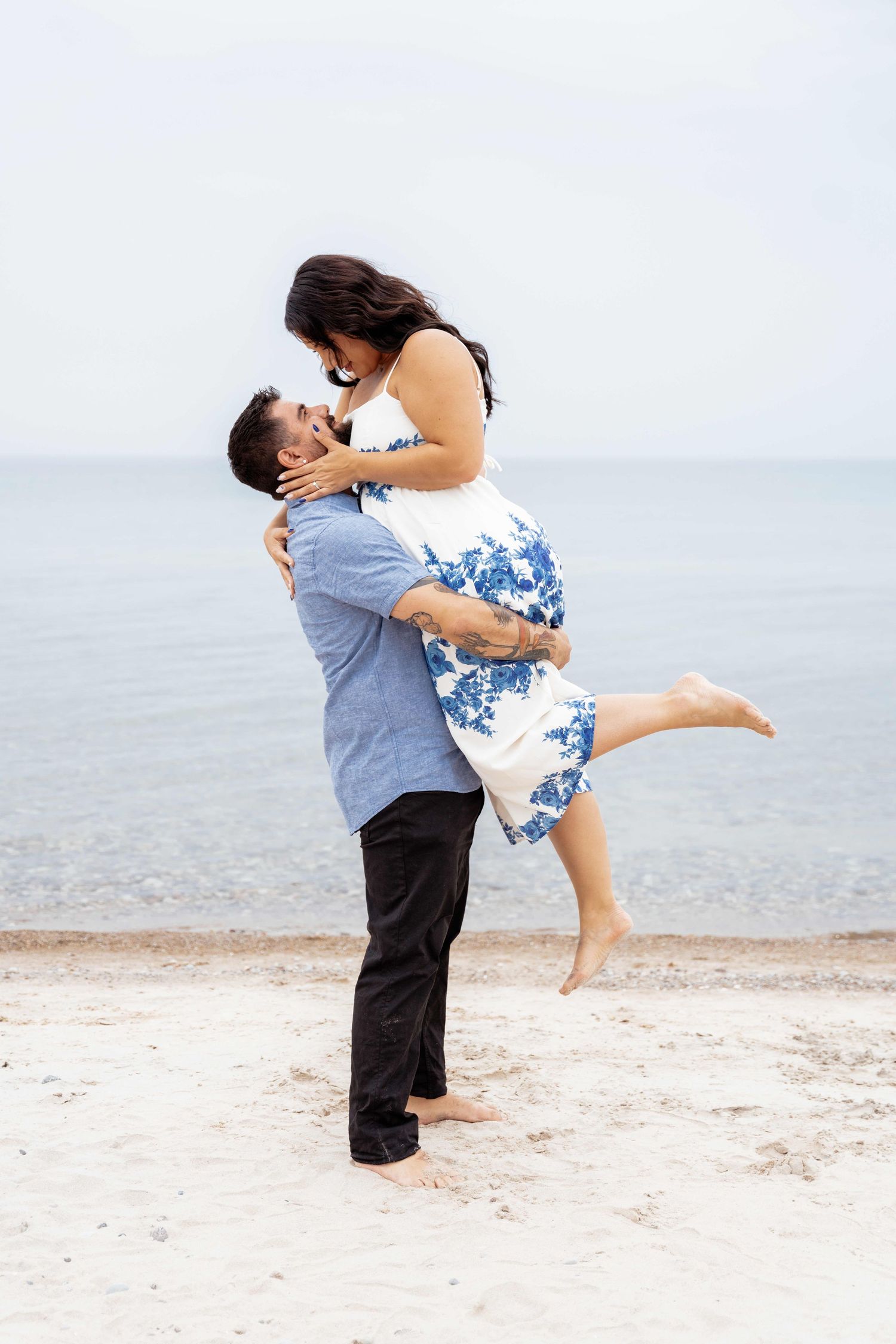 A couple embraces in a romantic moment on a serene beach with the ocean in the background.