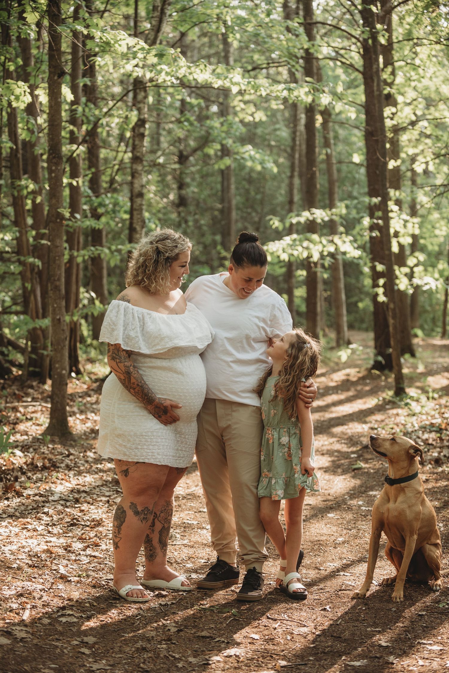 Family and their dog share tender moments in a sunlit forest path during an outdoor photo session.