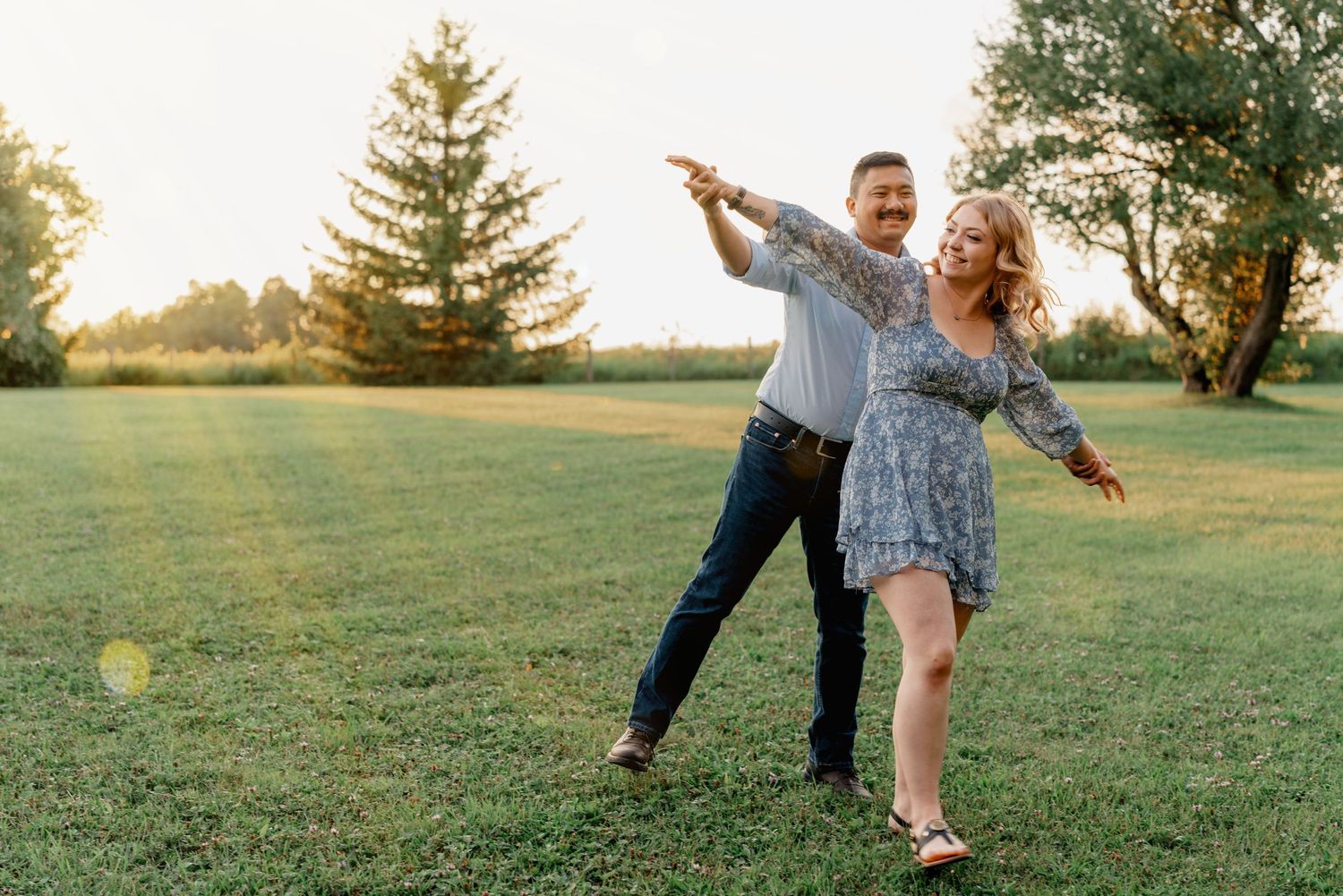 A couple dances together in a grassy field at sunset creating a romantic silhouette against the golden sky.
