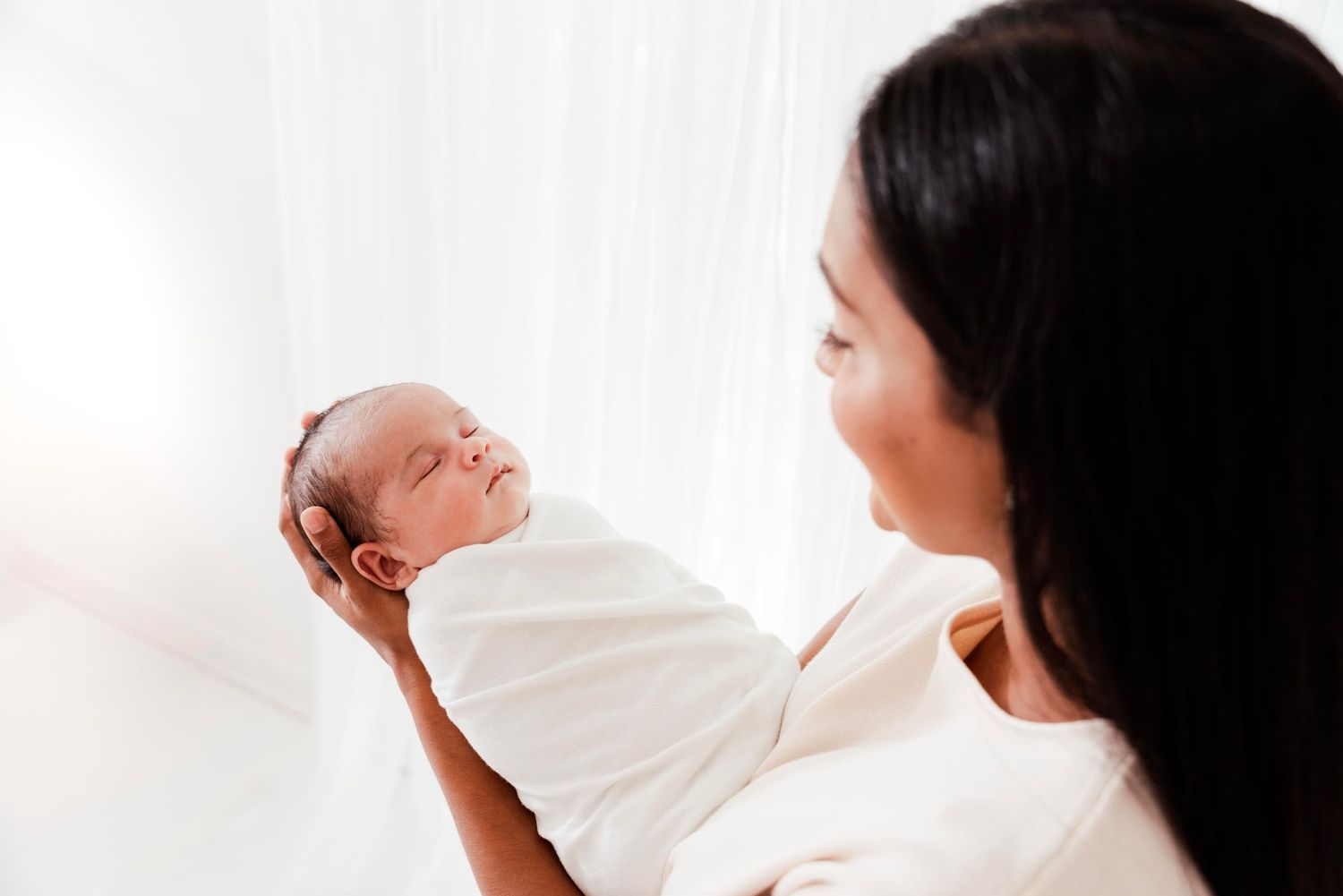 A mother and baby share a tender moment together during a nursing session in a bright, naturally lit room.