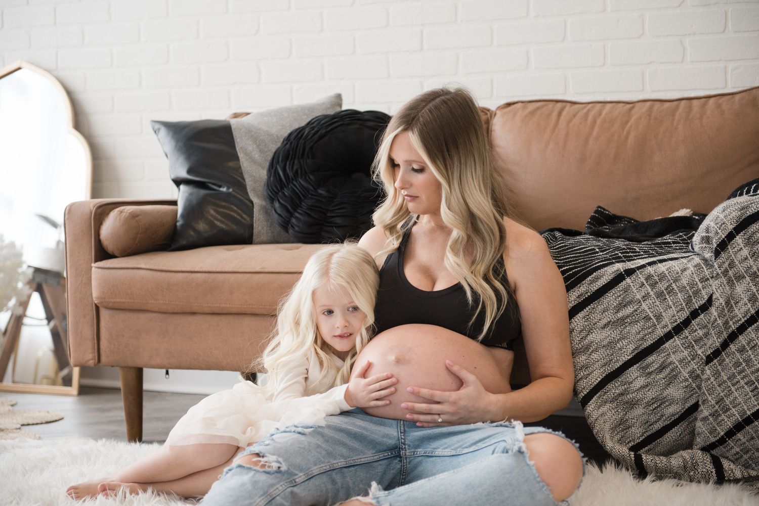 A person and baby share a tender moment on a couch with soft lighting and neutral decor in the background.