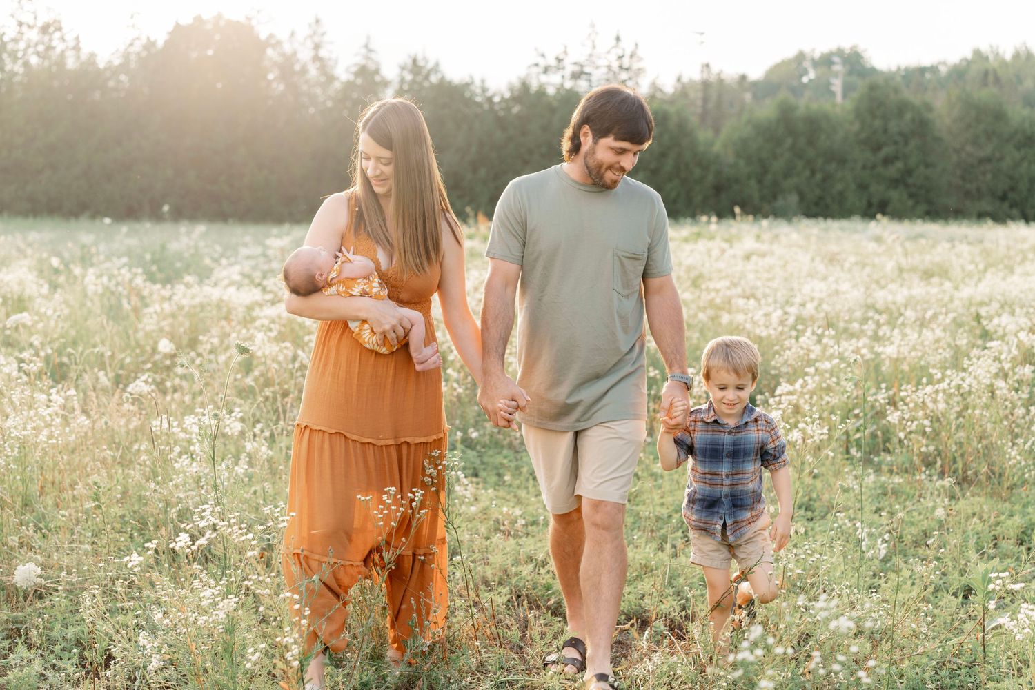 Family walks together through a sunlit meadow of wildflowers during golden hour.