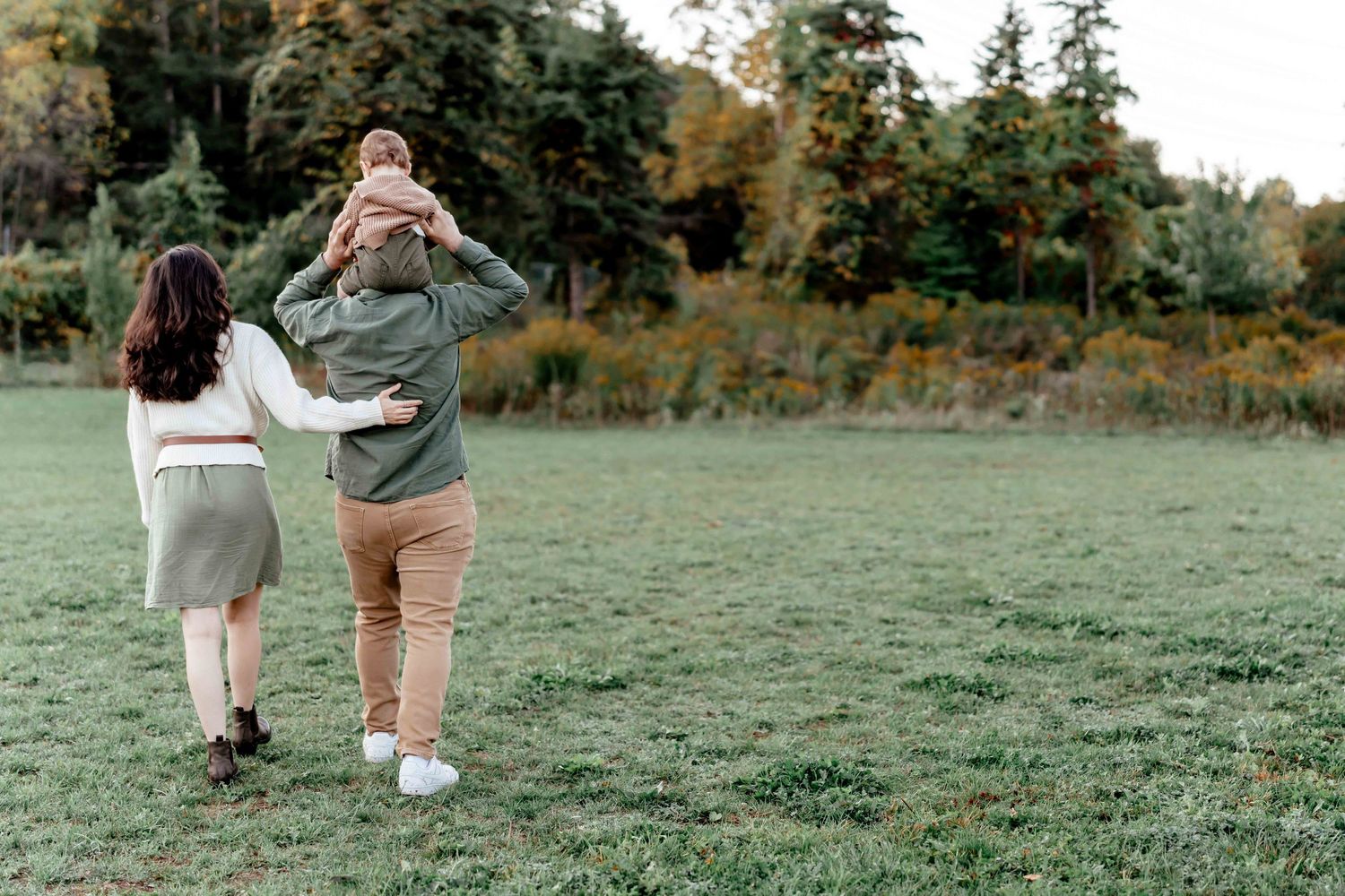 Two figures walk together on a grassy field during an autumn day in a romantic engagement photo session.